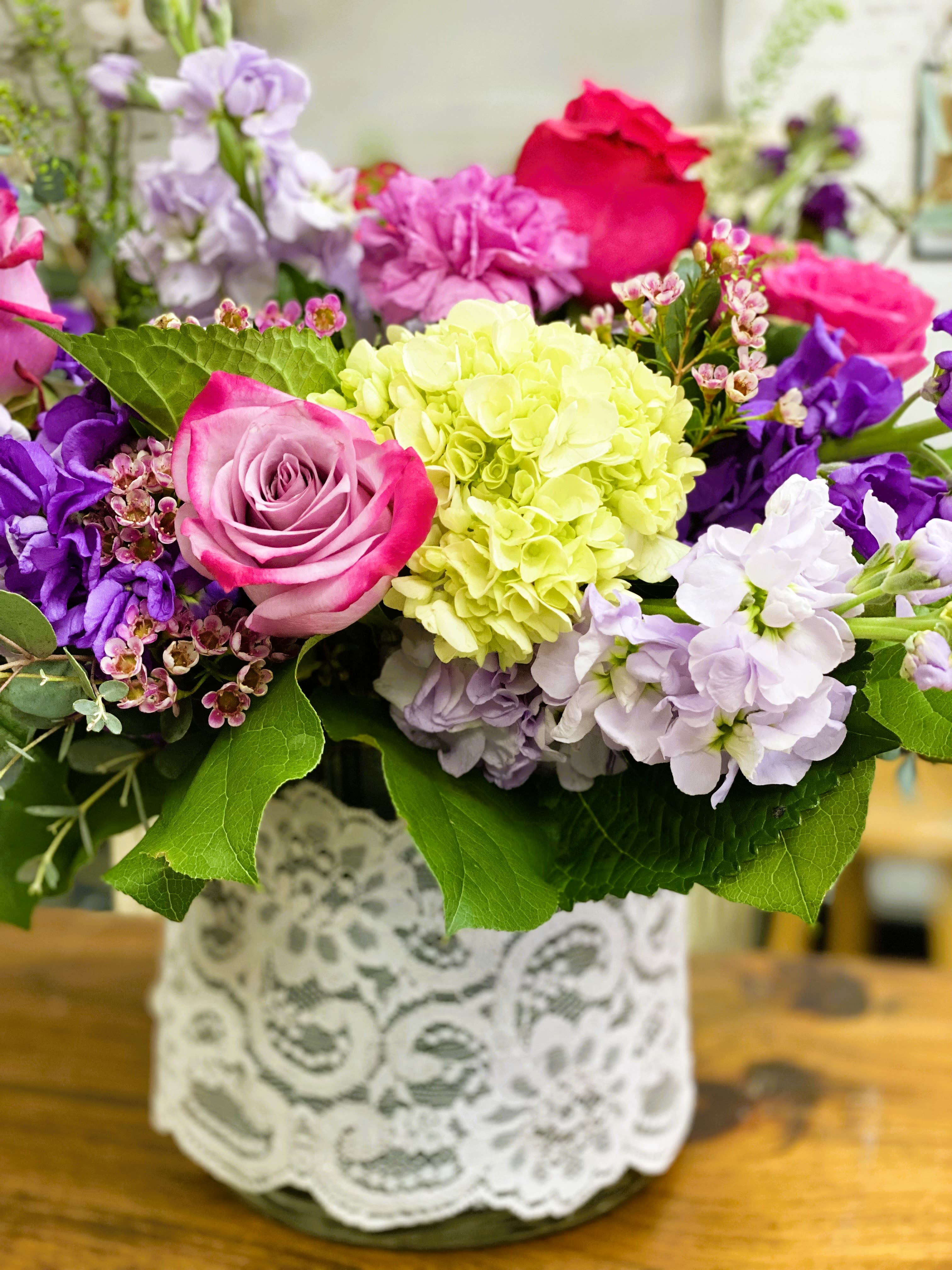 Mixed bouquet of pink, purple, and white flowers in a lace-wrapped vase