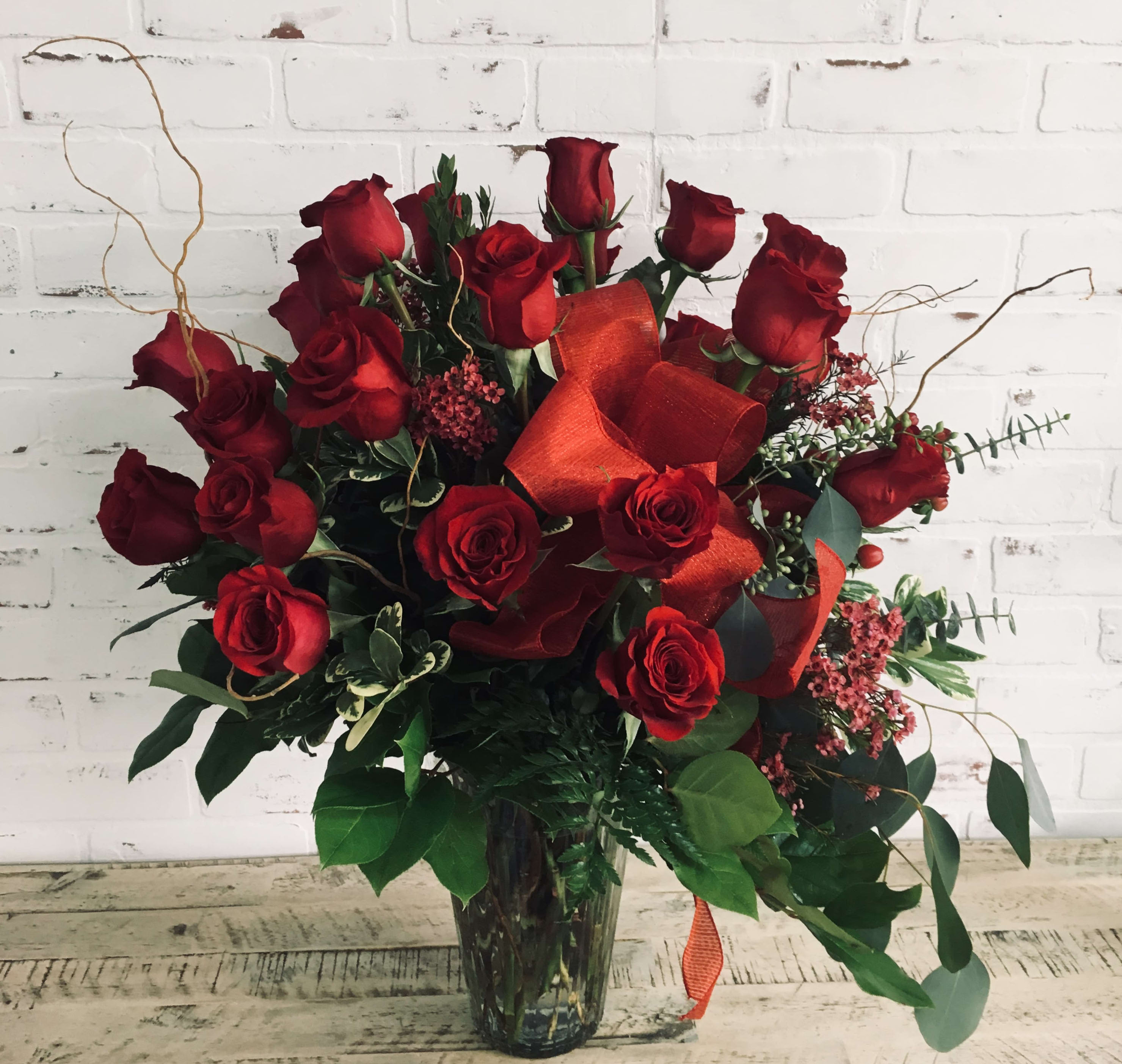 Red roses arranged in a clear glass vase with orange ribbon accents