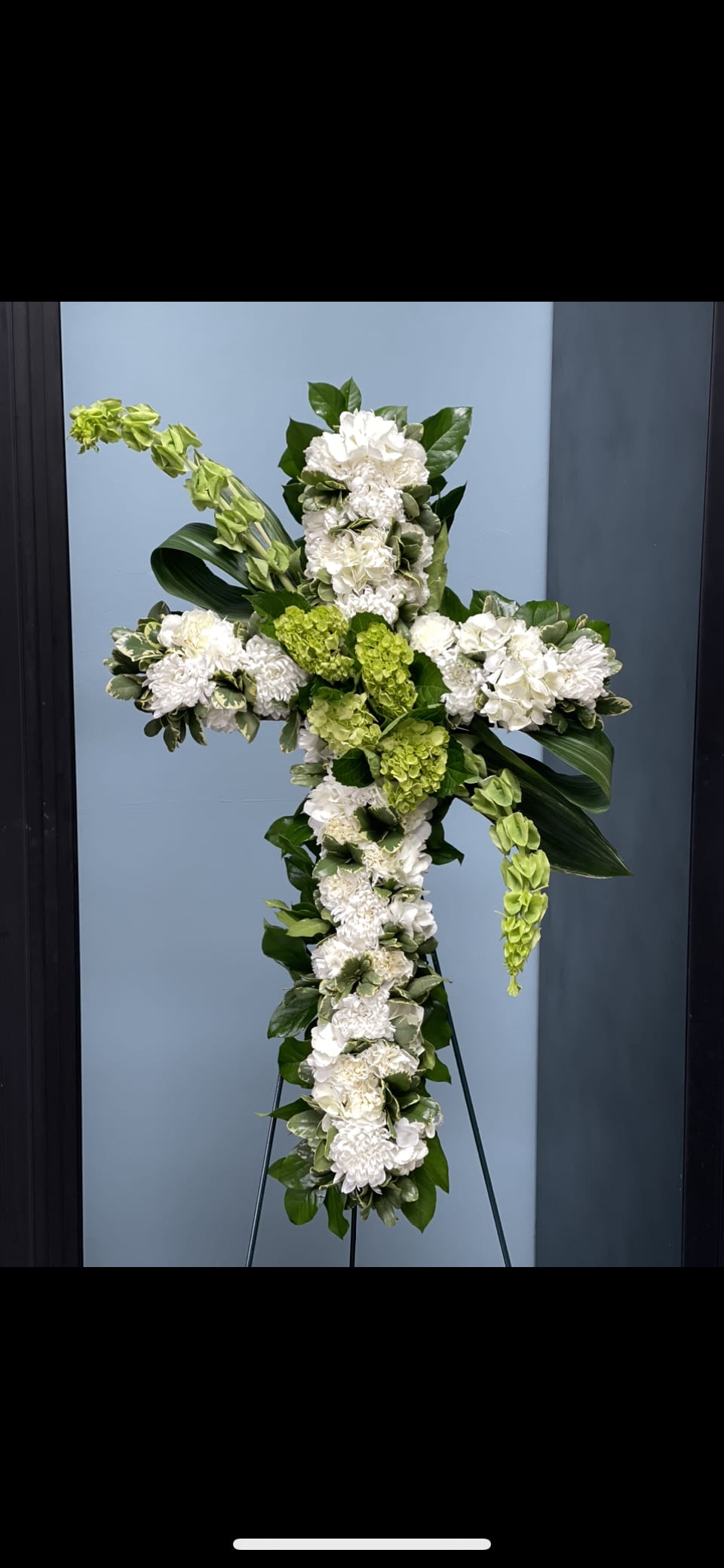 White and green floral cross arrangement on a stand