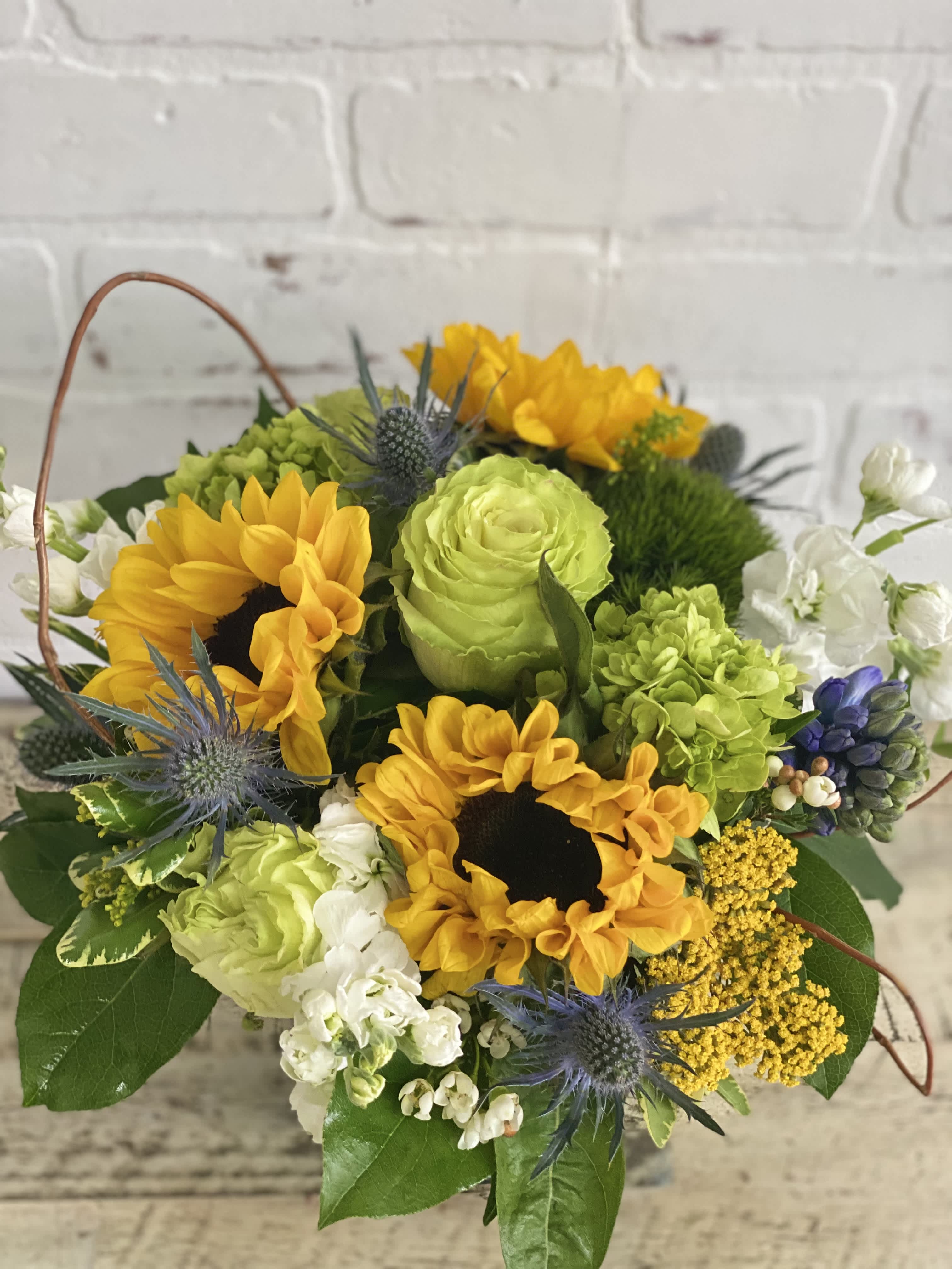 Basket arrangement with yellow sunflowers, green roses, and blue thistles