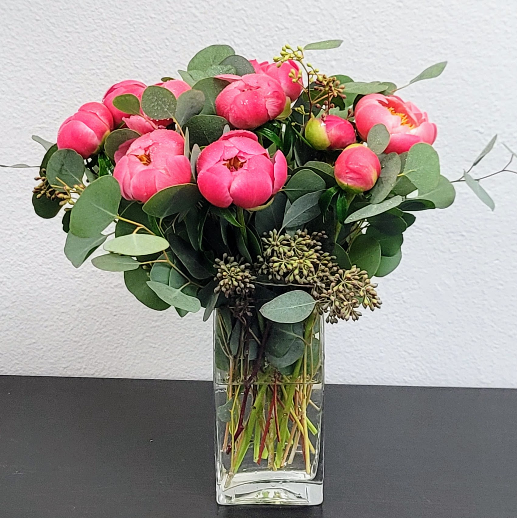 Pink peonies arranged in a clear glass vase with round eucalyptus leaves.