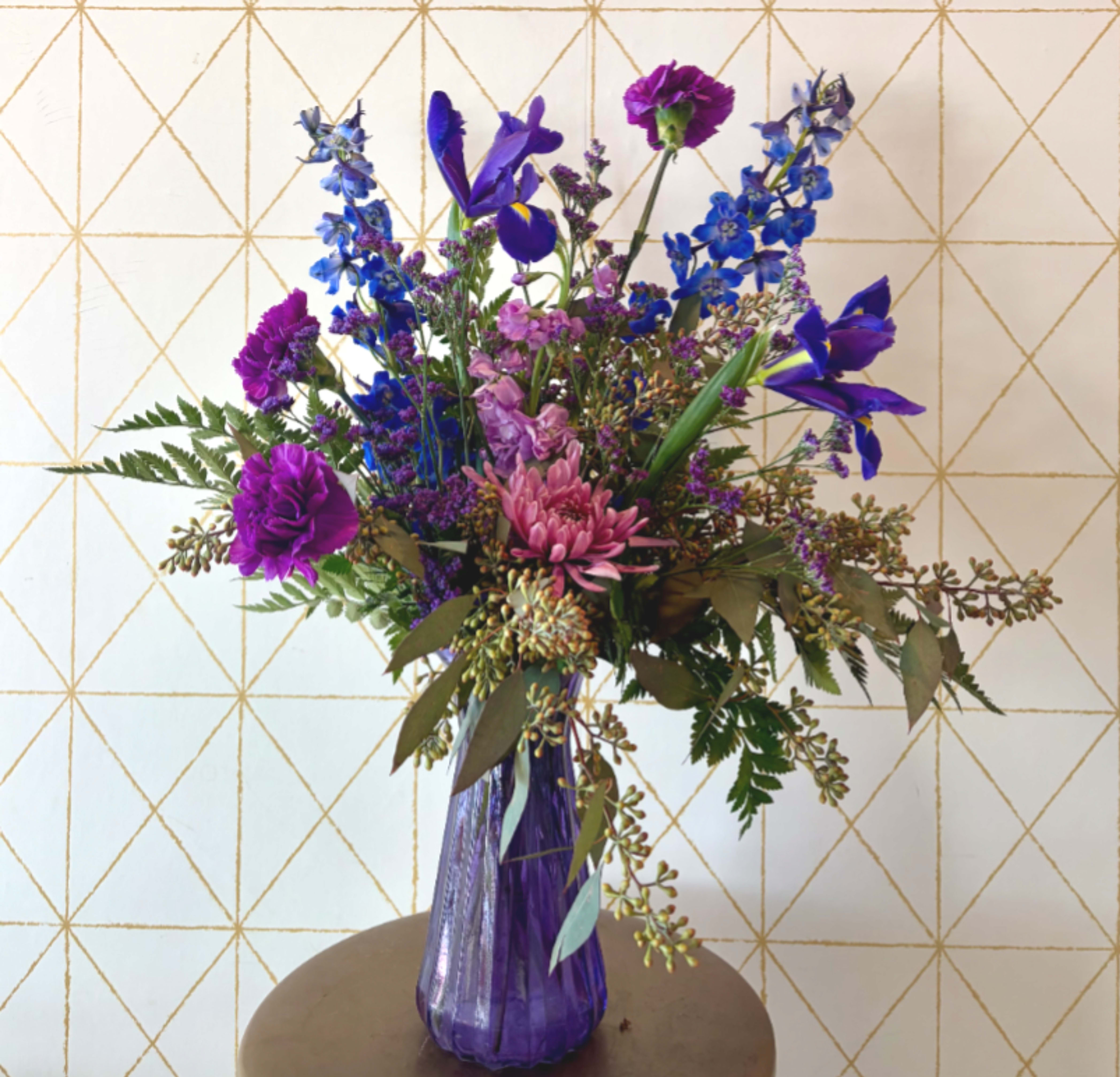 Purple and blue mixed flower arrangement in a tall purple vase