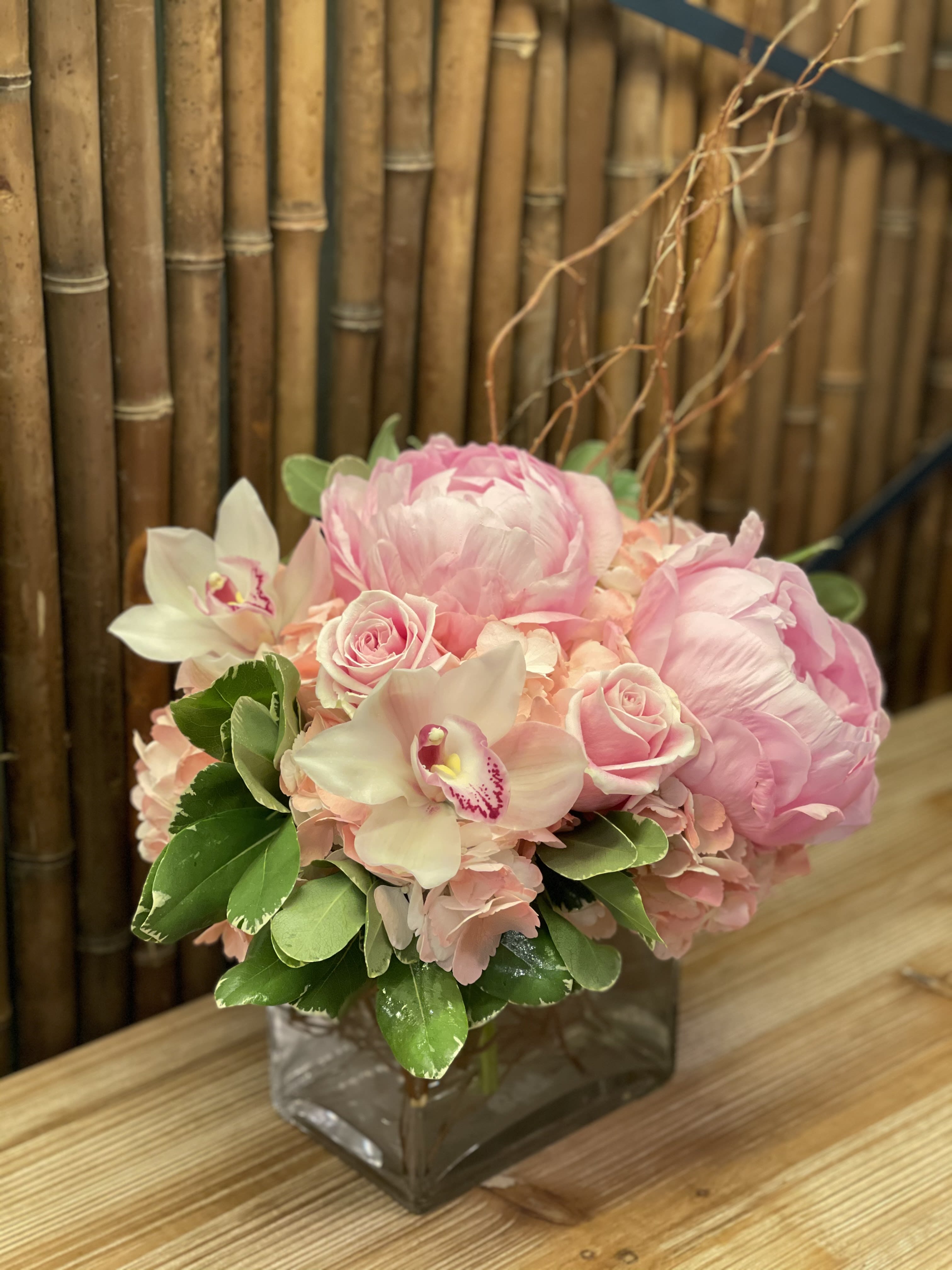 Pink floral arrangement in a square glass vase with roses and orchids