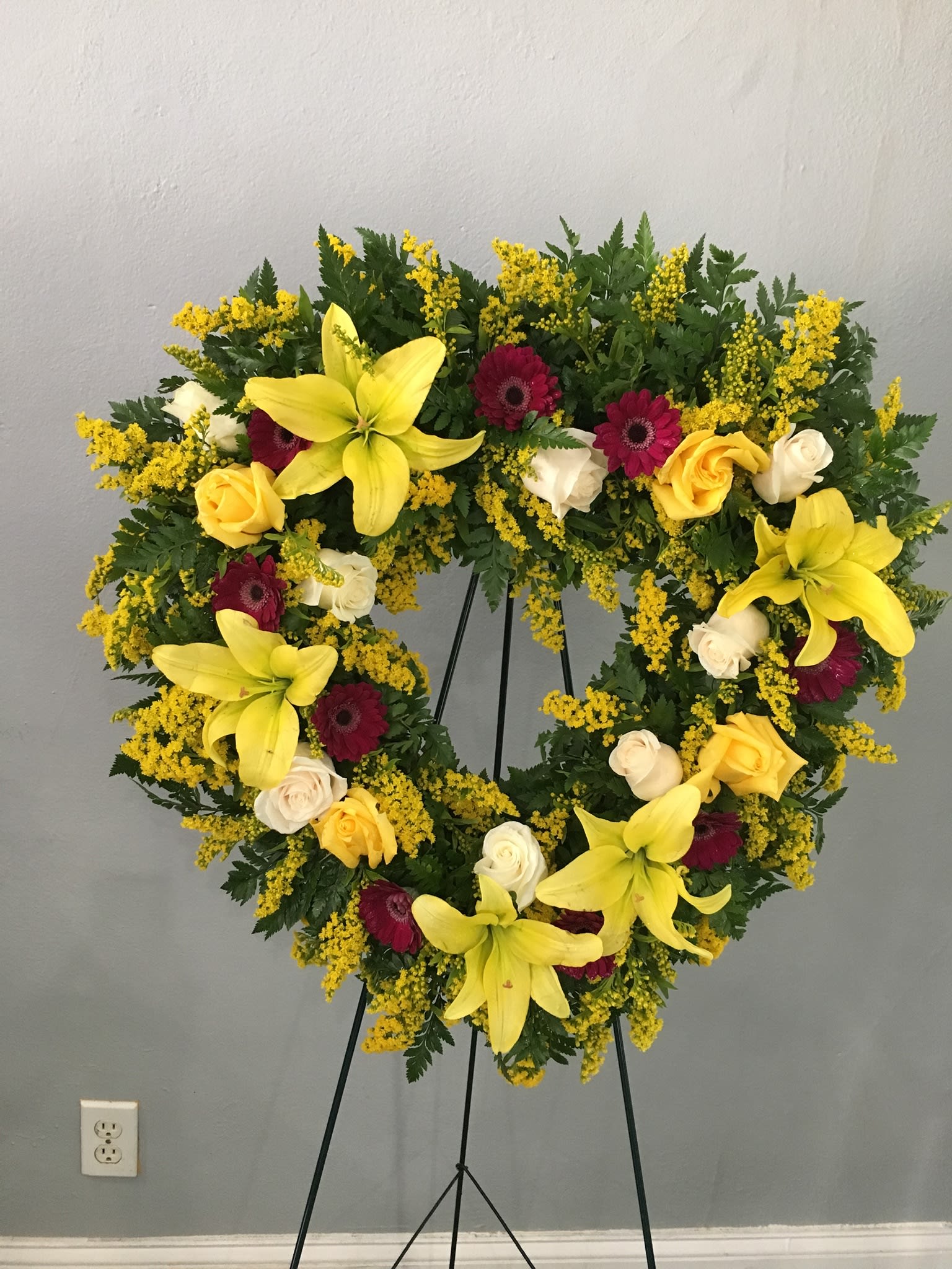 Heart-shaped floral wreath with yellow lilies, roses, and burgundy gerberas