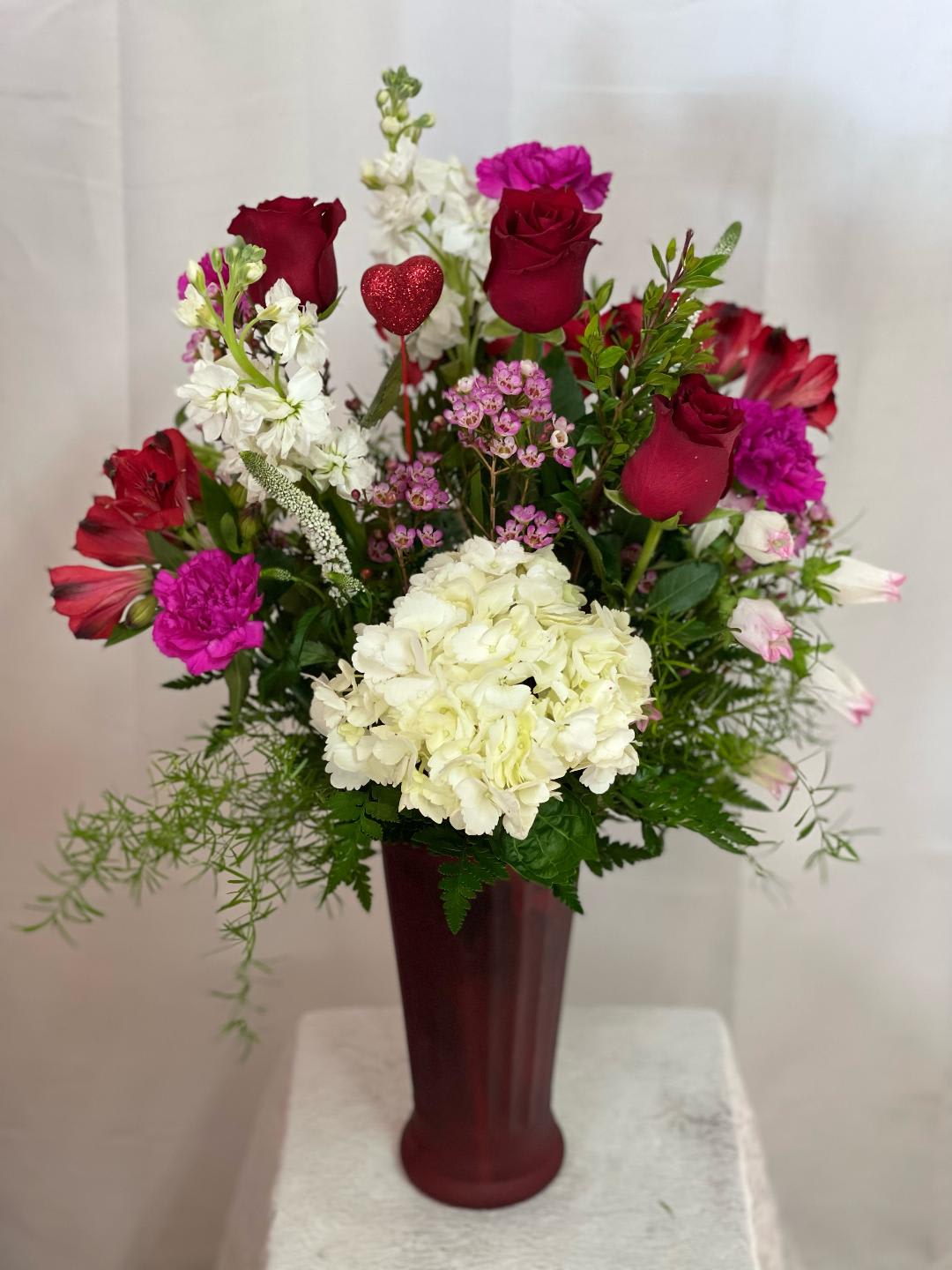 Mixed bouquet of red roses, white hydrangea, and pink flowers in a tall vase