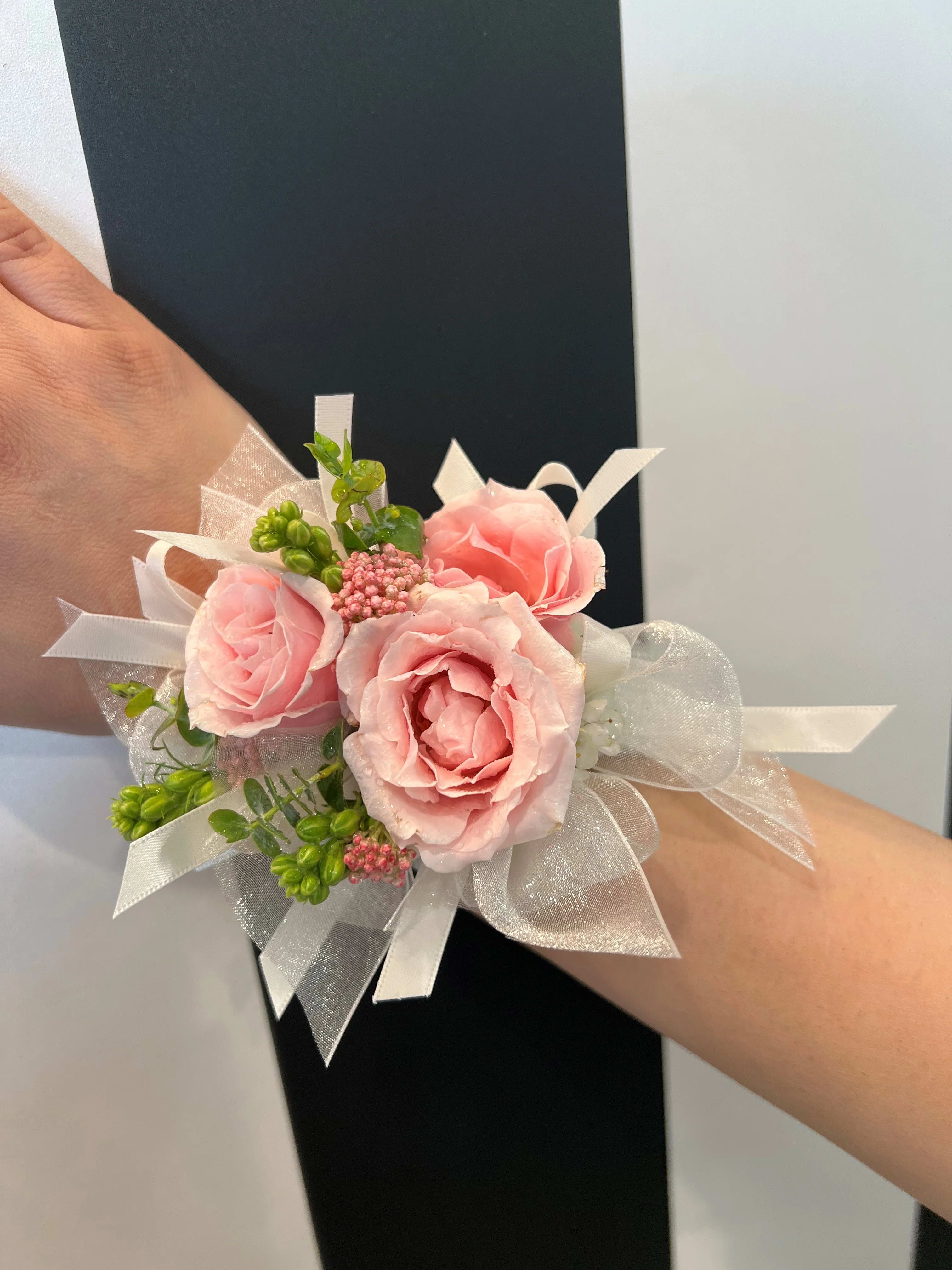 Pink rose wrist corsage with white ribbon and green accents
