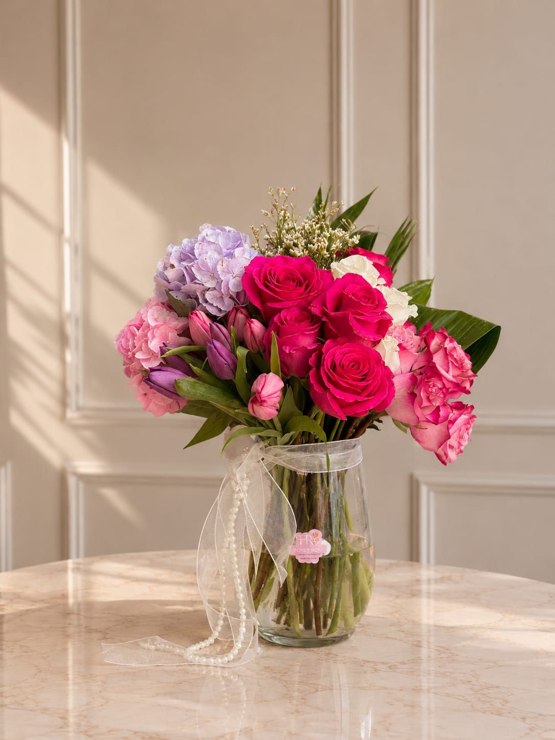 Velvet Charm  - An elegant arrangement featuring premium roses, tulips, hydrangeas, and fresh greenery designed in a clear glass vase for a soft and luxurious look.