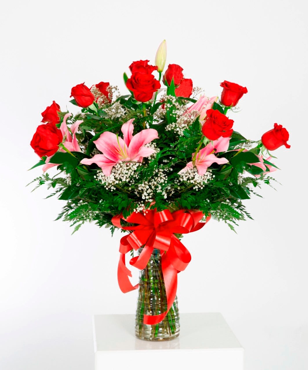 Red roses and pink lilies in a glass vase with a red ribbon