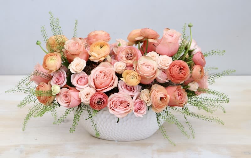 Low centerpiece of peach and pink roses and ranunculus in a white ceramic bowl