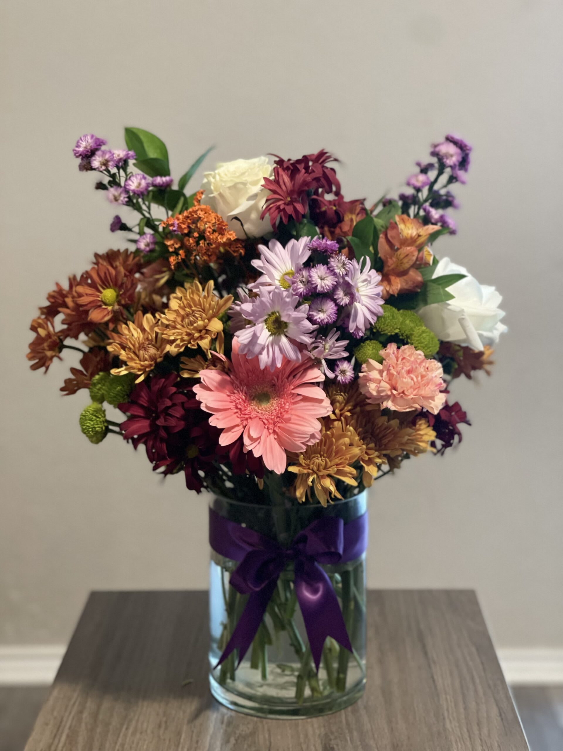 Mixed bouquet of chrysanthemums and roses in a glass vase with a purple ribbon