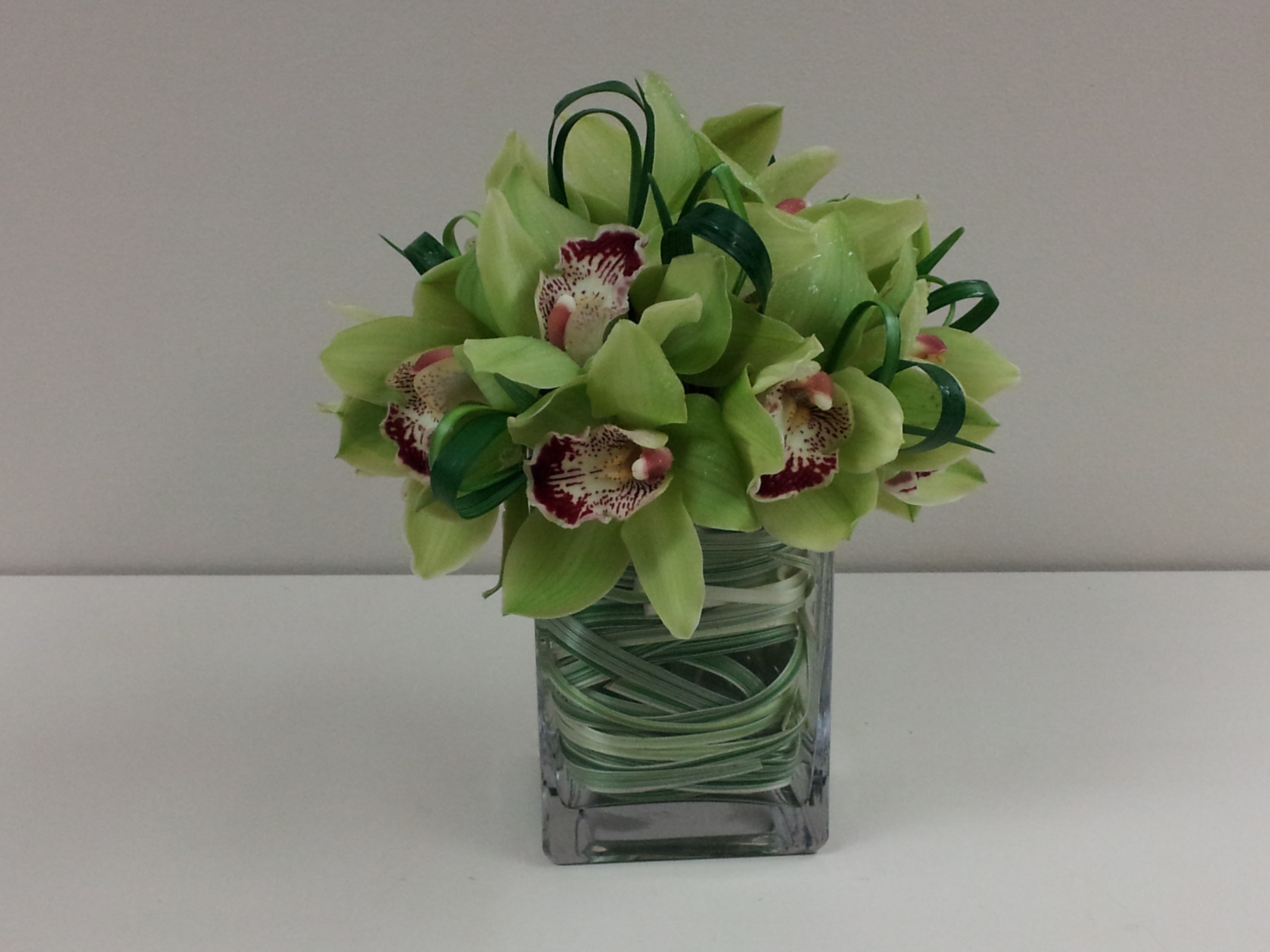 Green orchid bouquet in a square glass vase