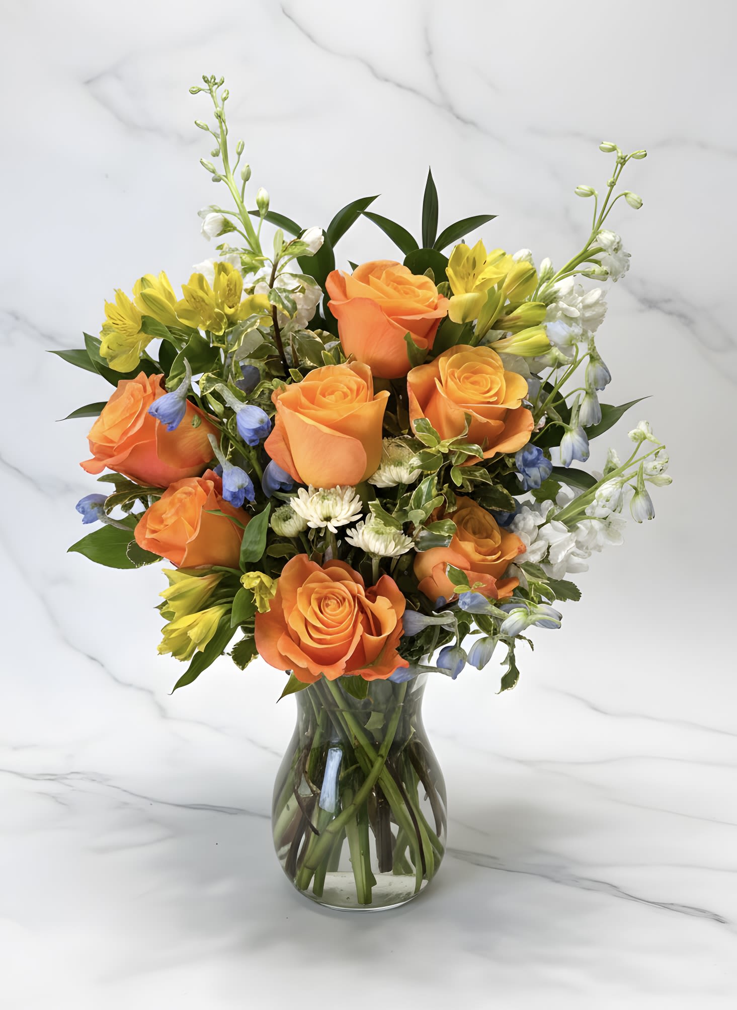 Mother's Sunset  - A Bright and Sunny Floral Arrangement of Orange Roses, Yellow Alstromeria, Light Blue Delphinium and white floral accents and a varitety of greenery. 
