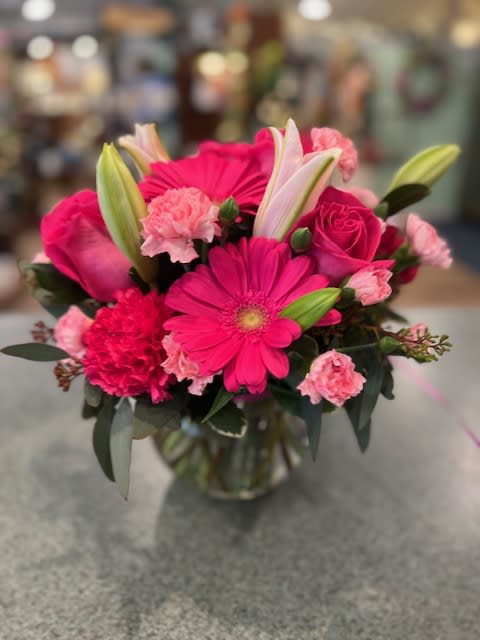 Compact bouquet of bright pink gerbera daisies, roses, carnations, and lilies in a clear glass vase