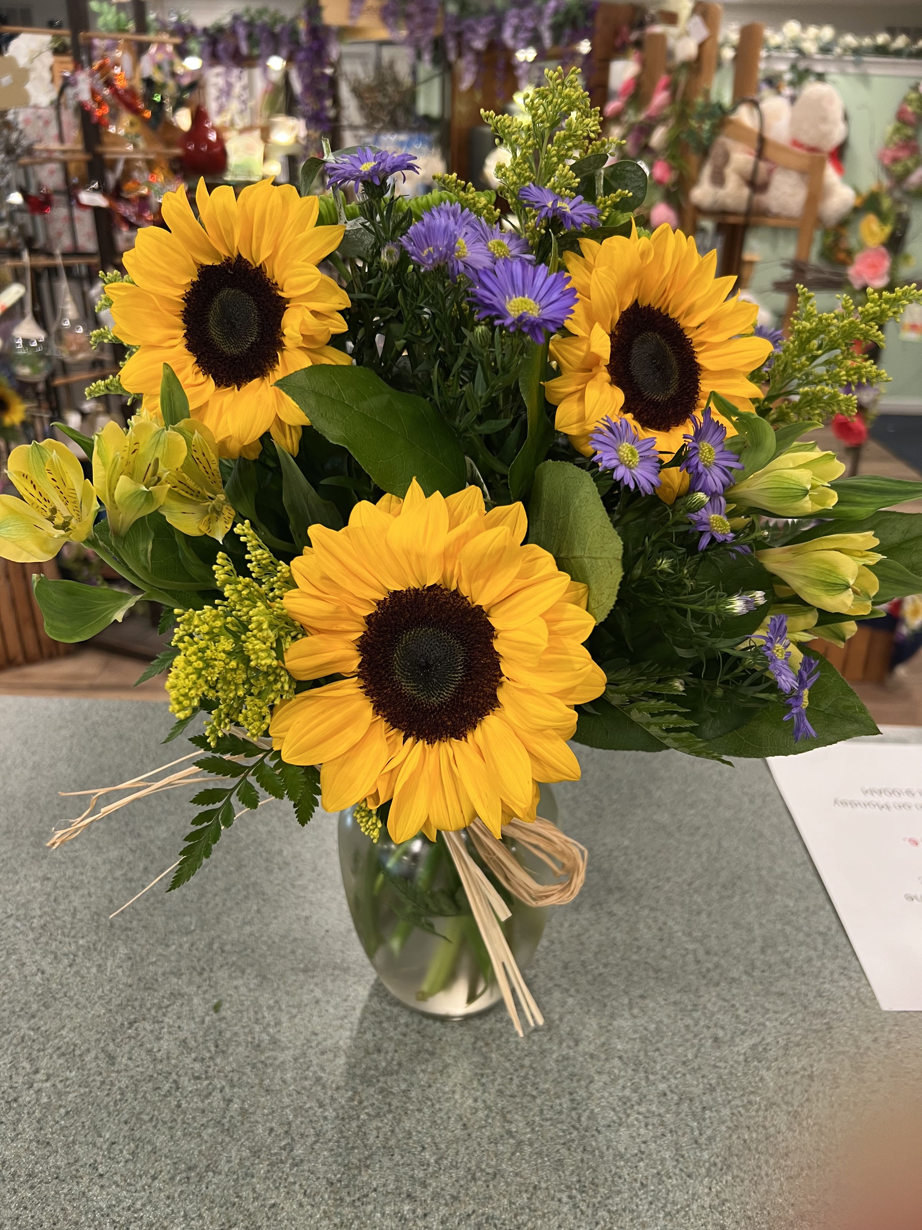 Bouquet of sunflowers, purple asters, and yellow lilies in a glass vase