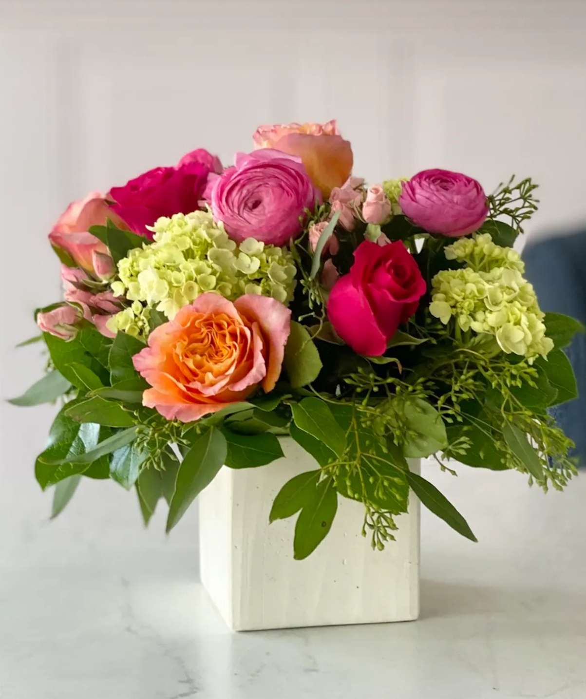Pink and orange roses with pale green hydrangeas in a white vase