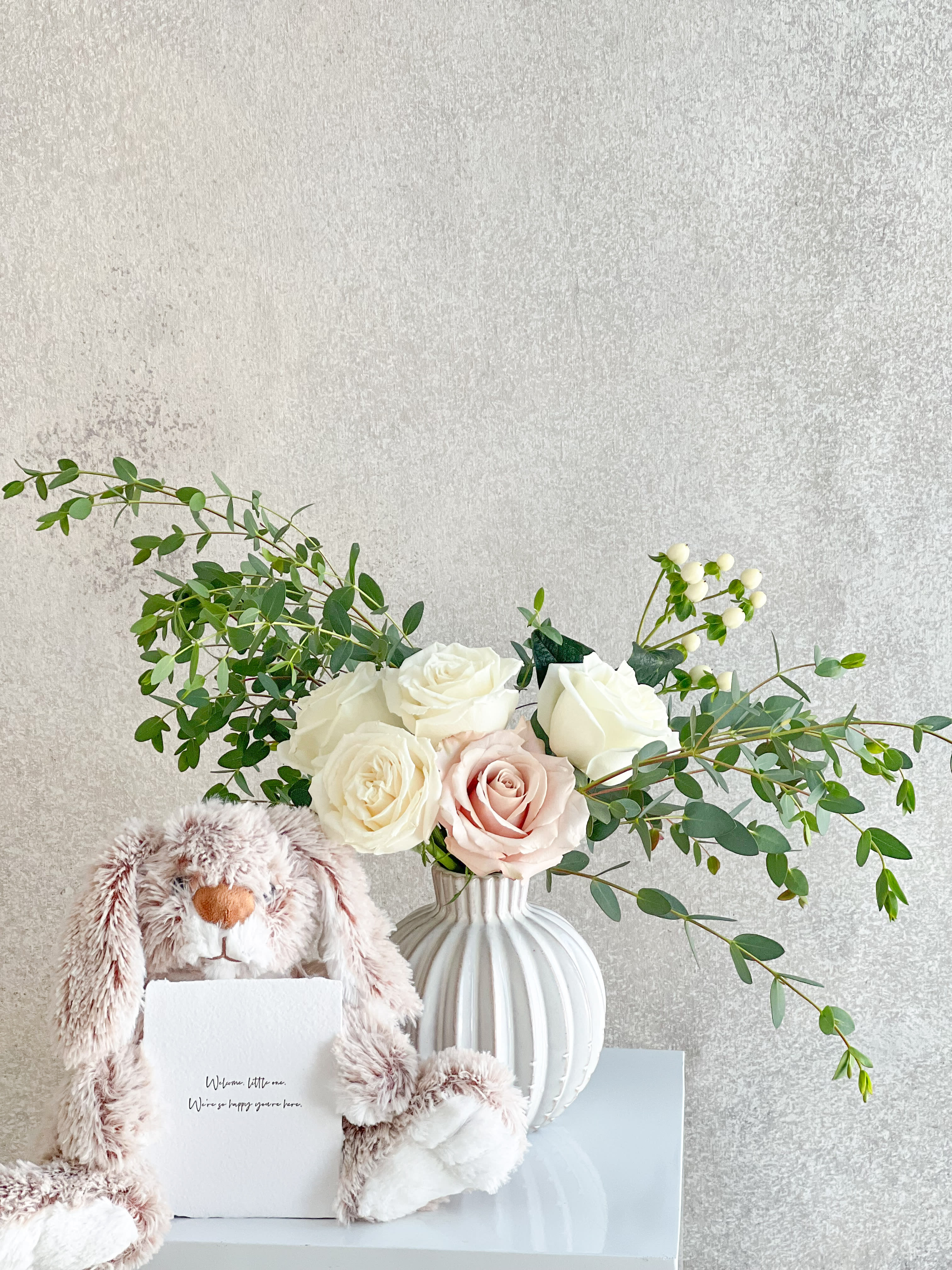White and blush roses in a ribbed vase with a plush bunny and card