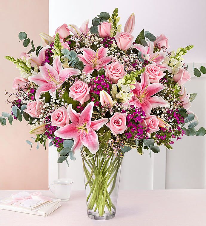 Tall glass vase filled with pink lilies, roses, and white accent flowers.