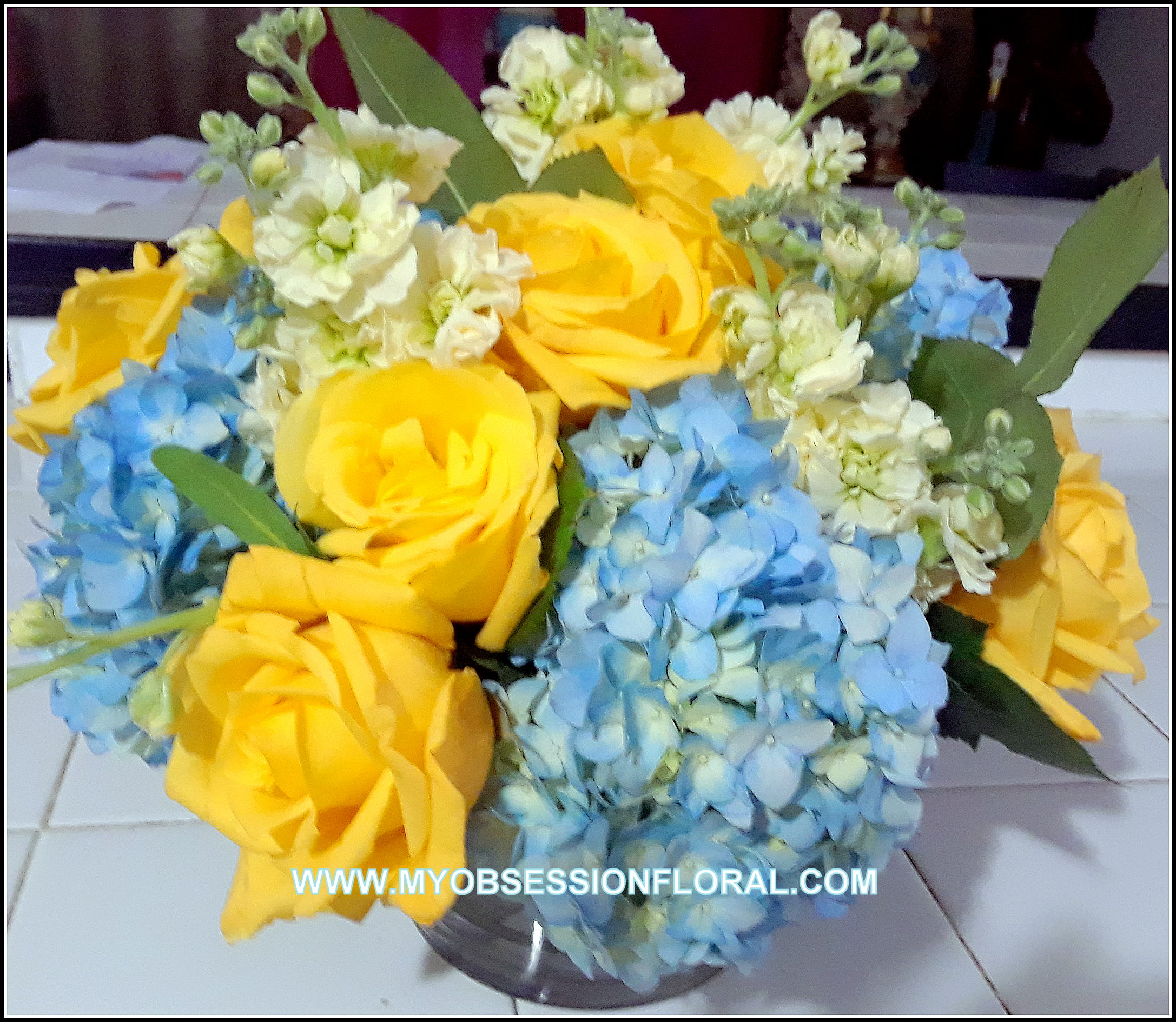 Bouquet of yellow roses and blue hydrangeas in a clear vase