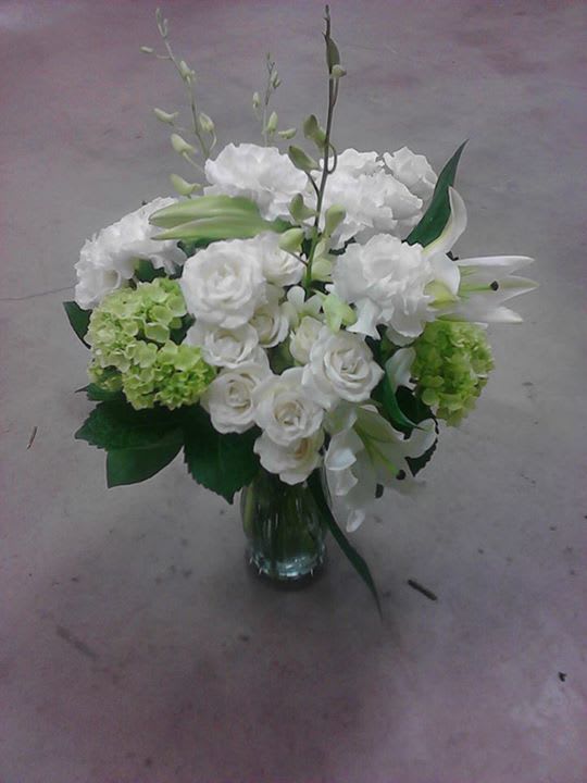 White floral arrangement in a glass vase with green accents