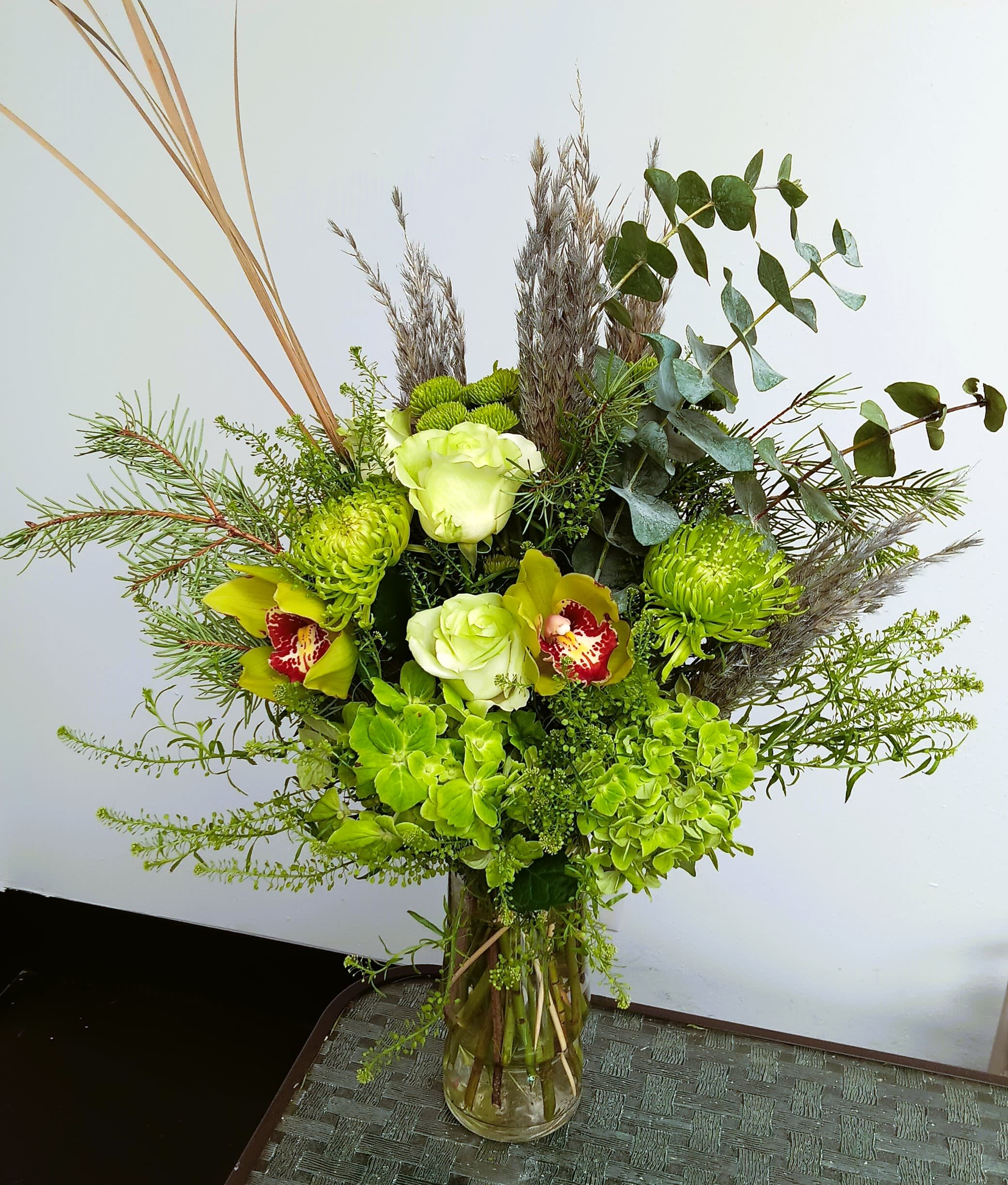 Green floral arrangement in a glass vase with orchids and hydrangeas
