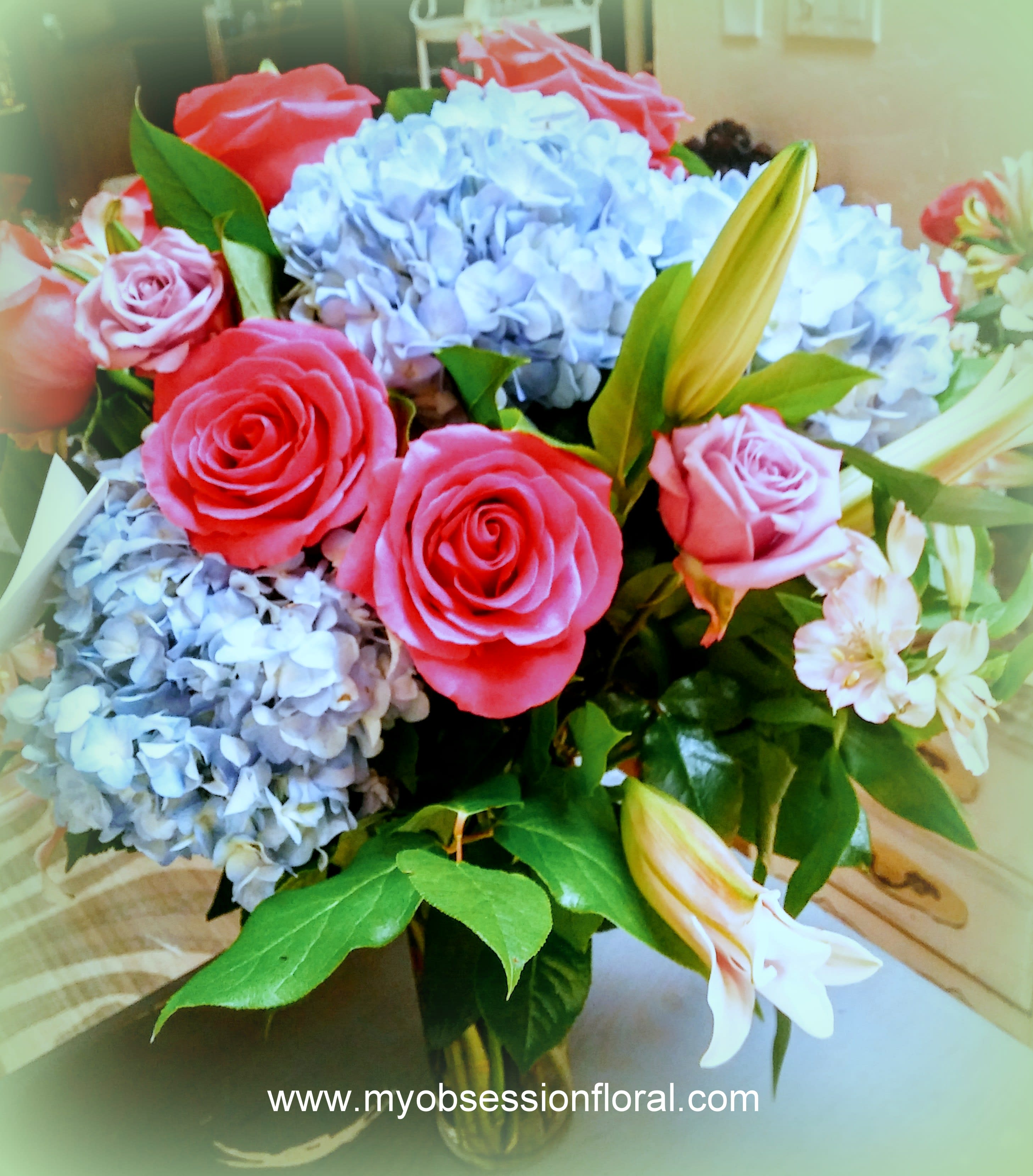 Bouquet of pink roses, blue hydrangeas, and white lilies in a glass vase