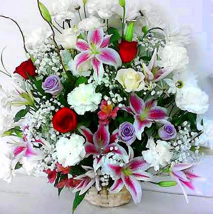 Mixed bouquet of white and pink lilies, red roses, and purple blooms in a vase