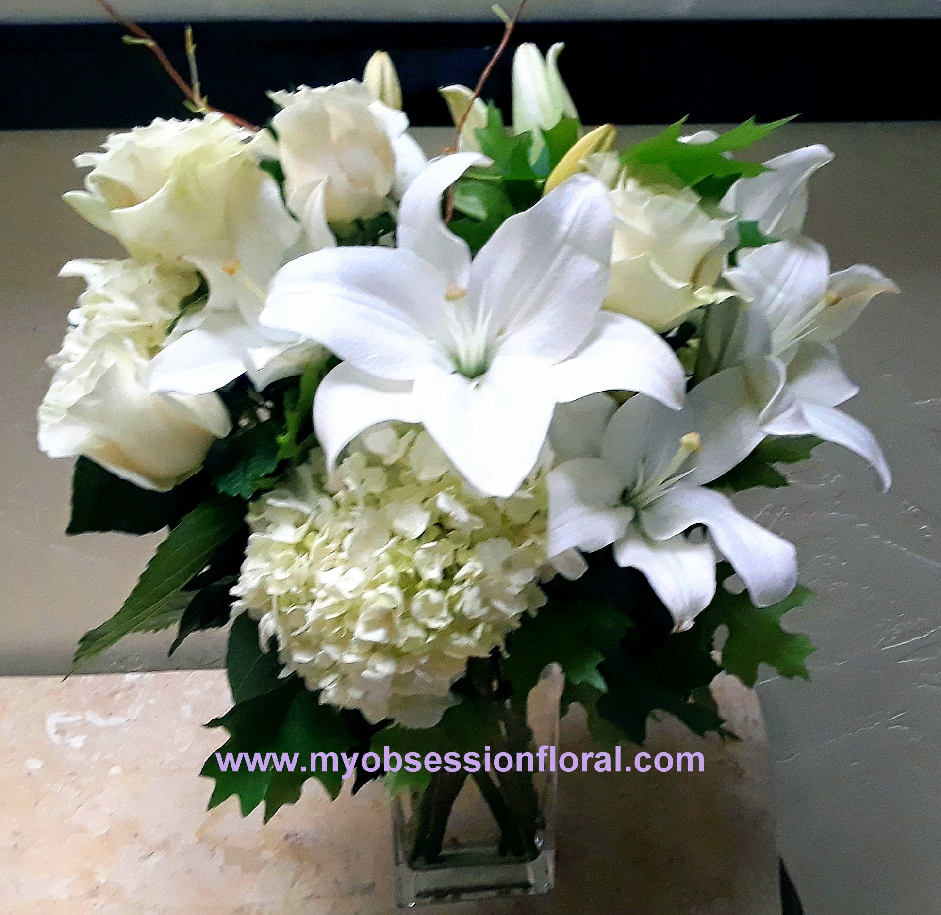 White lilies and roses arranged in a clear glass vase