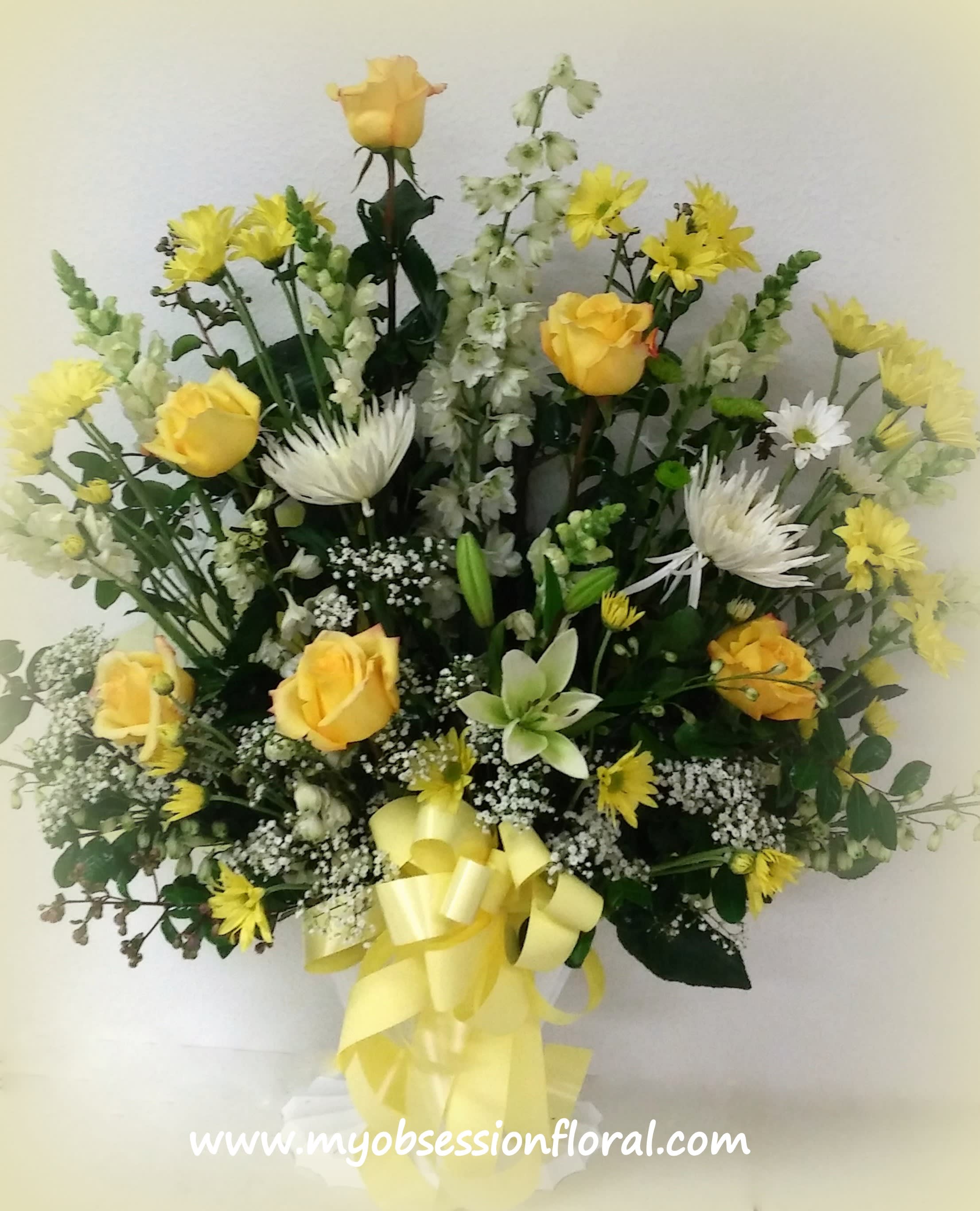 Yellow roses and white flowers arranged in a vase with a yellow ribbon