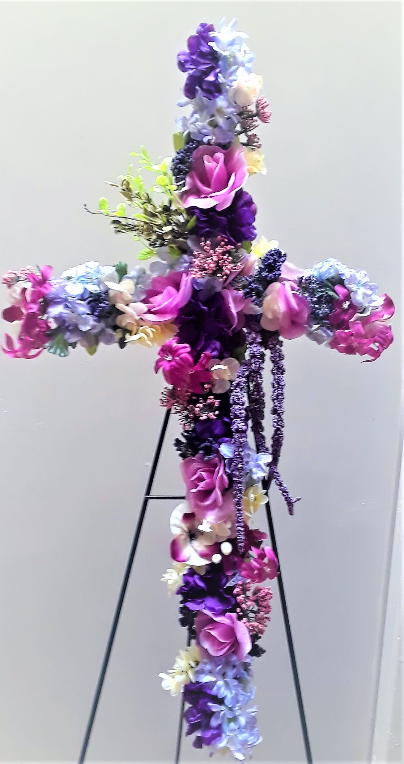 Cross-shaped floral arrangement in purple, pink, and white on a stand