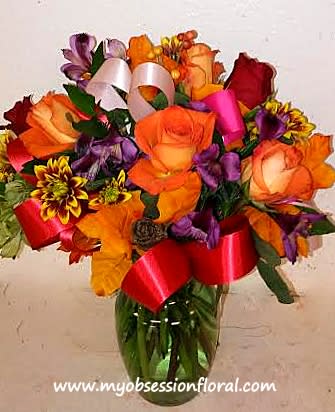 Bouquet of orange, red, and purple flowers in a glass vase with ribbons