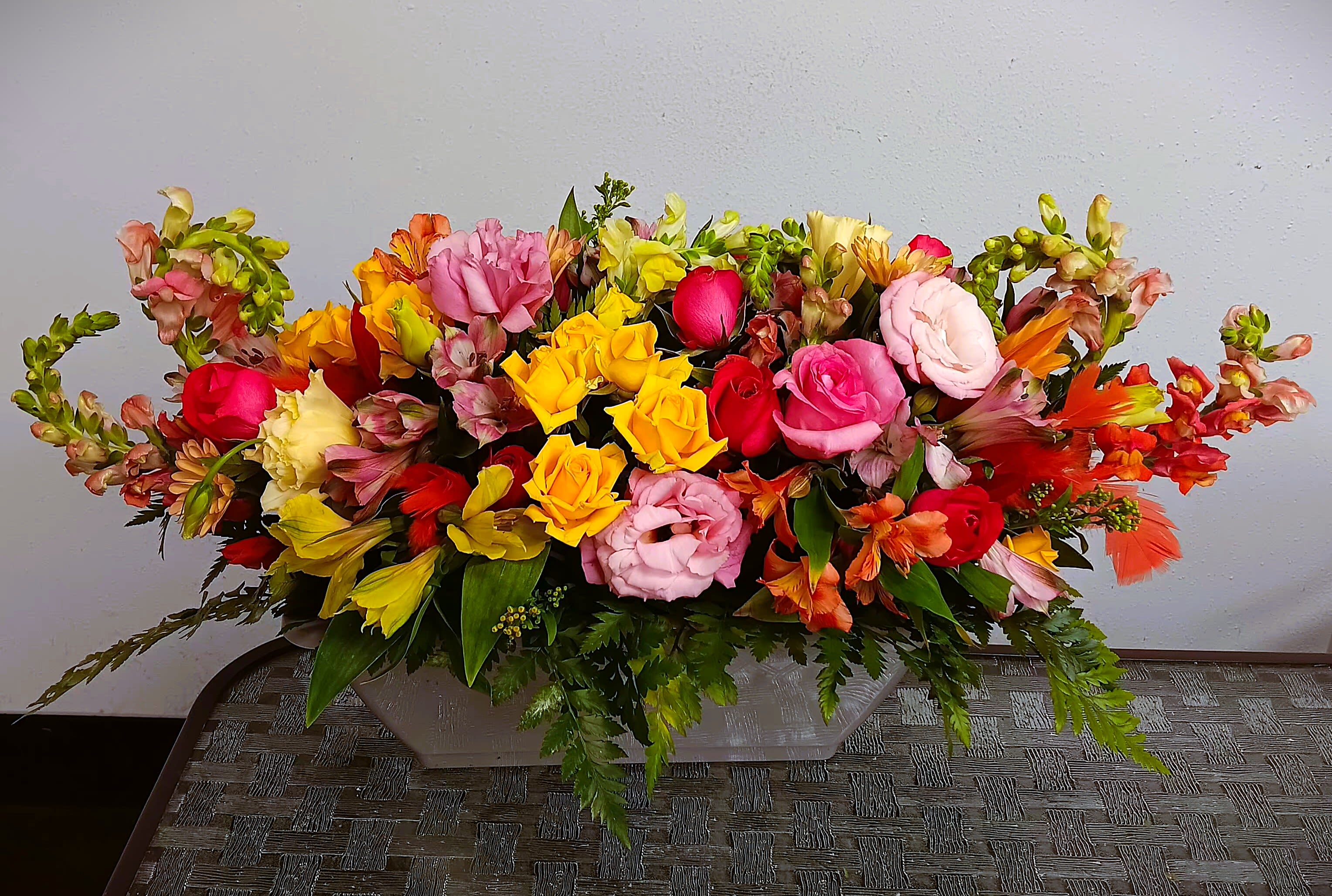 Long low arrangement of multicolored roses and alstroemeria in a rectangular container