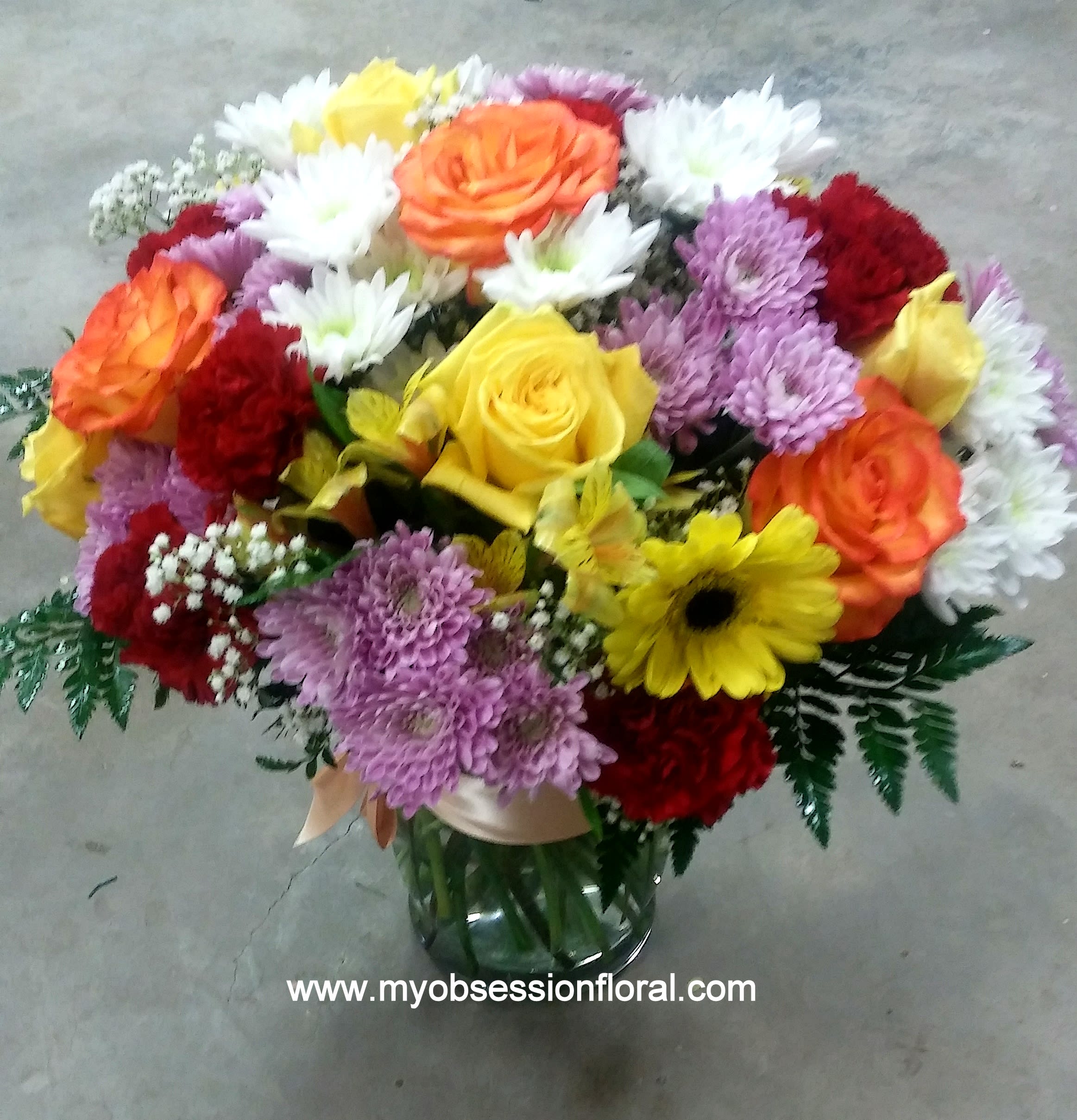 Mixed bouquet of roses, chrysanthemums, and daisies in a glass vase