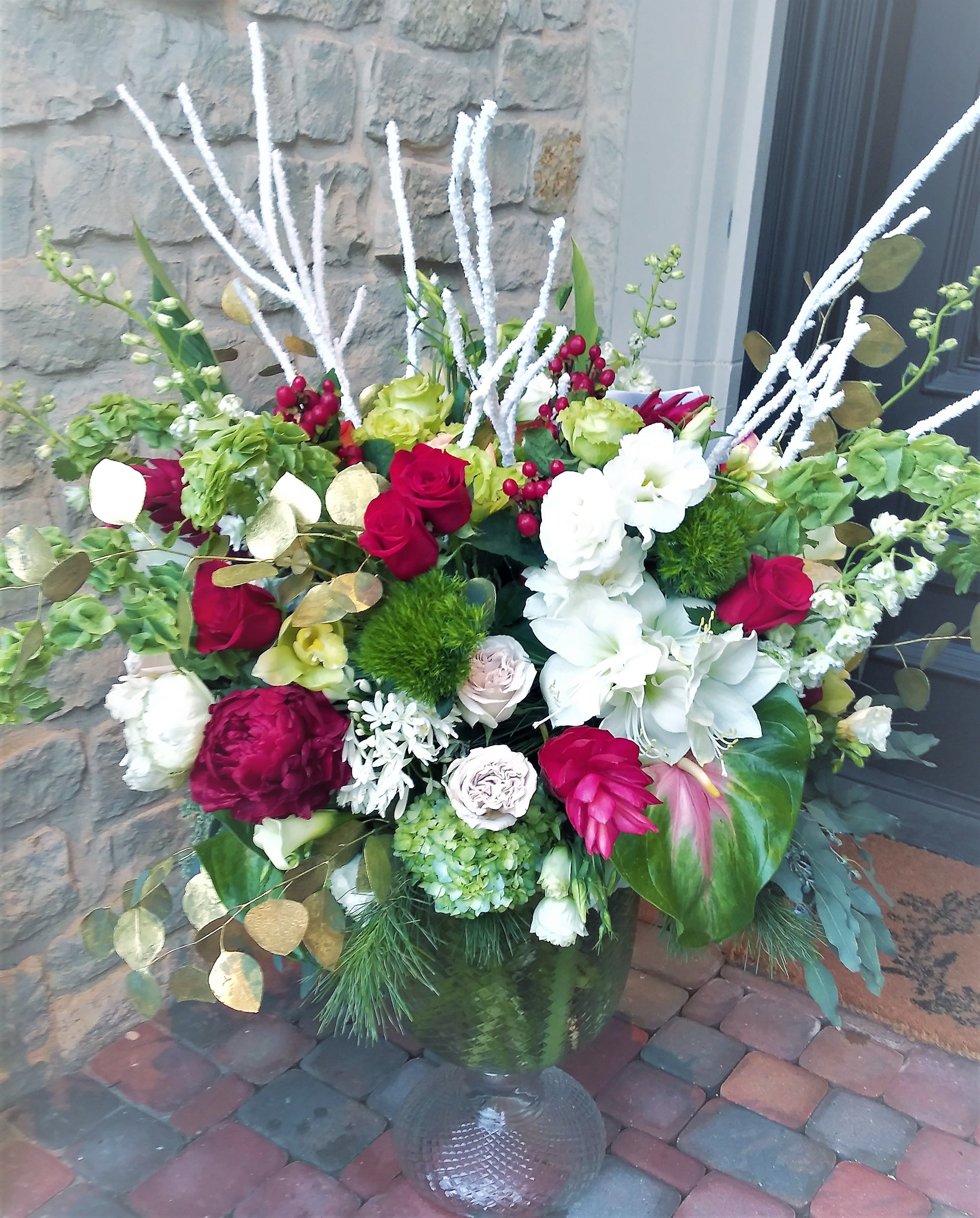 Large mixed floral arrangement in a glass vase with red, white, and green blooms
