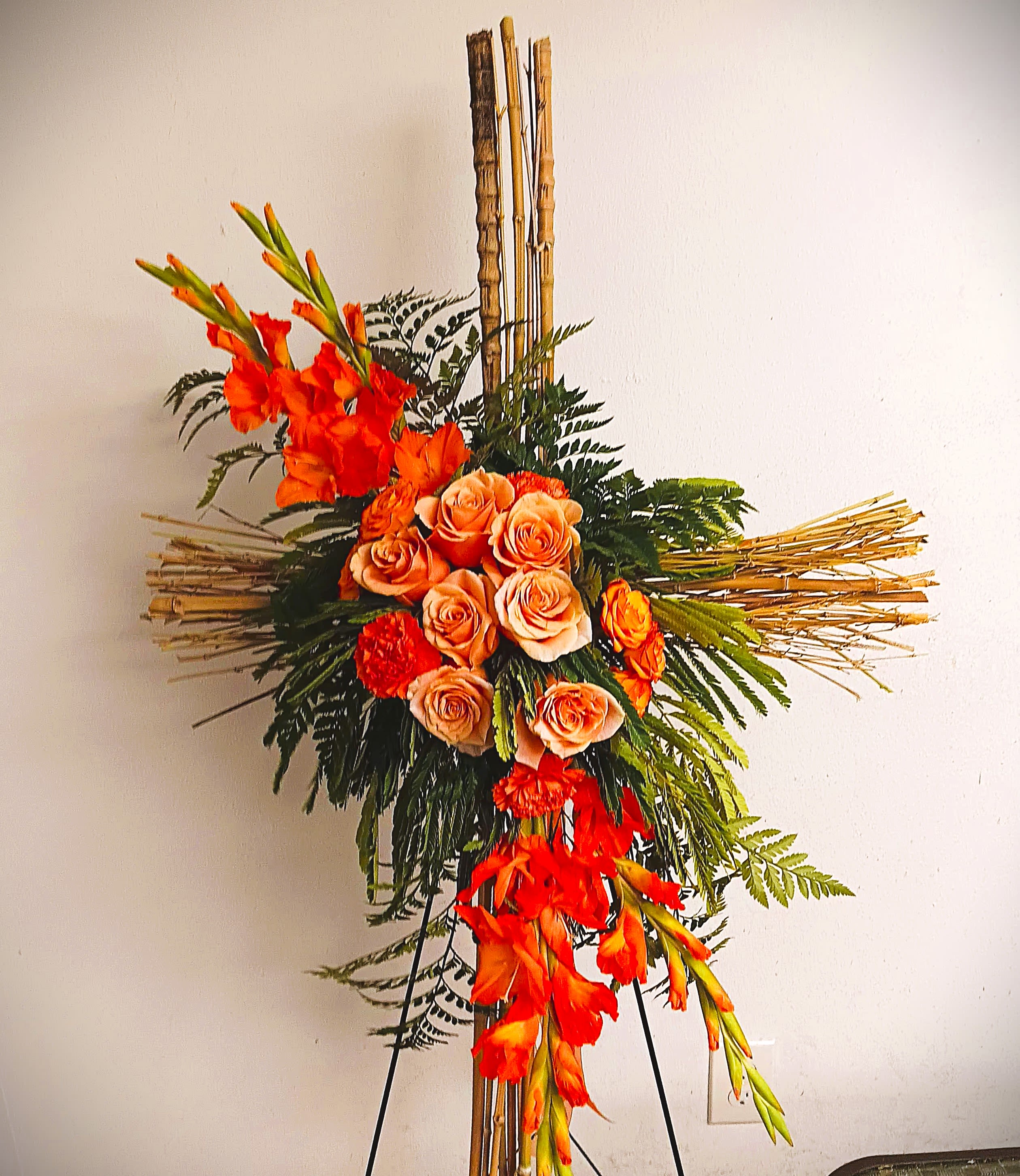 Tall floral arrangement with orange roses and gladiolus on a bamboo stand