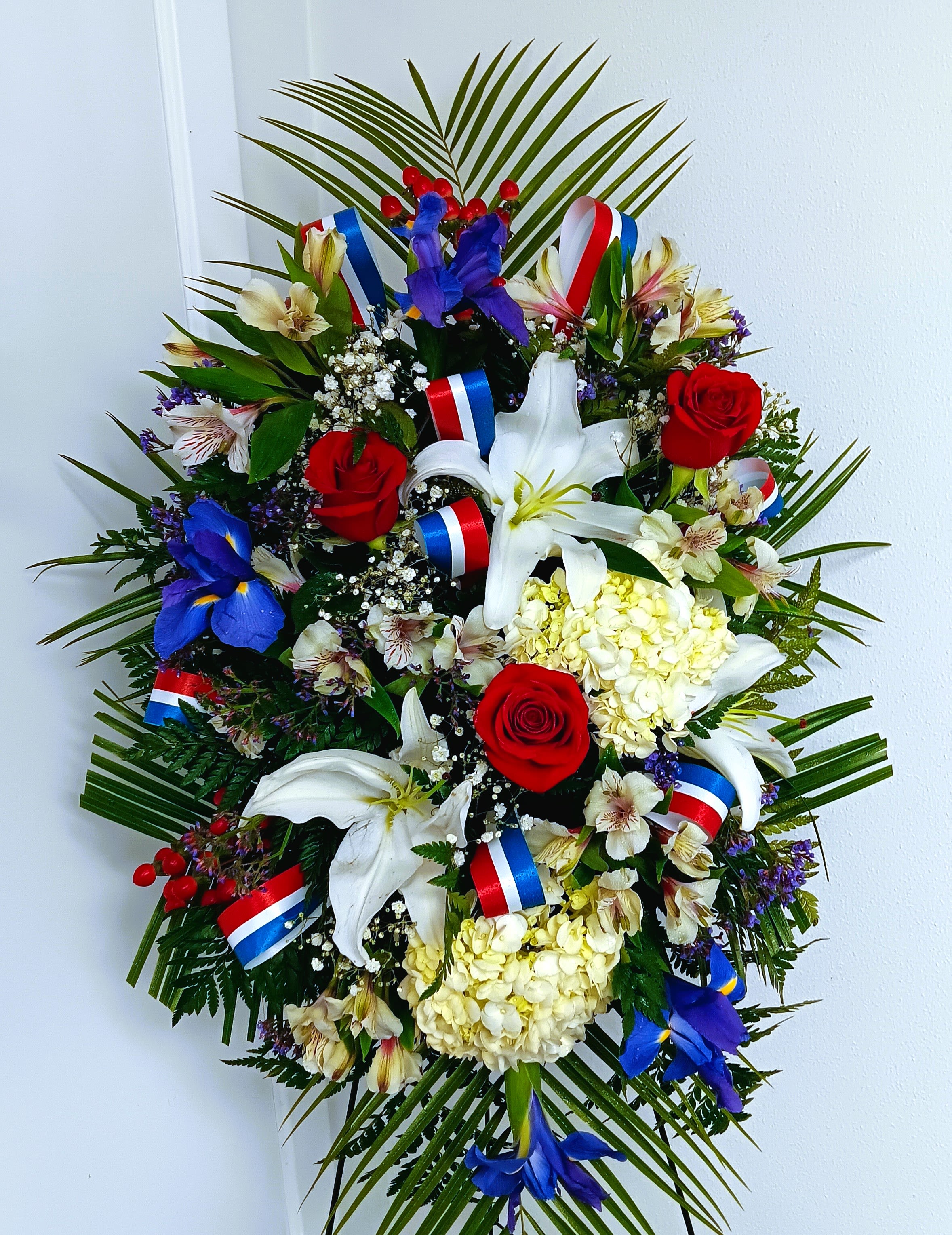 Large floral wreath with red roses, white lilies, and blue flowers