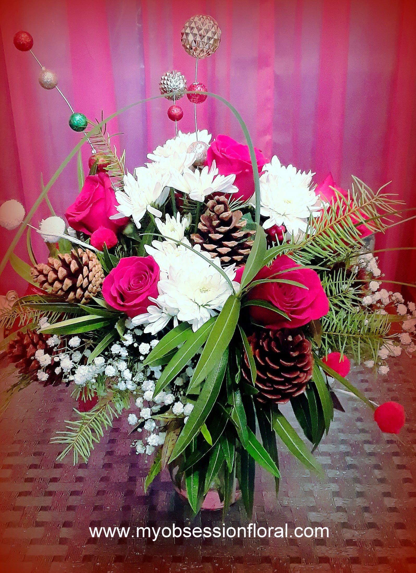 Pink roses and white daisies arranged with pinecones in a decorative basket.