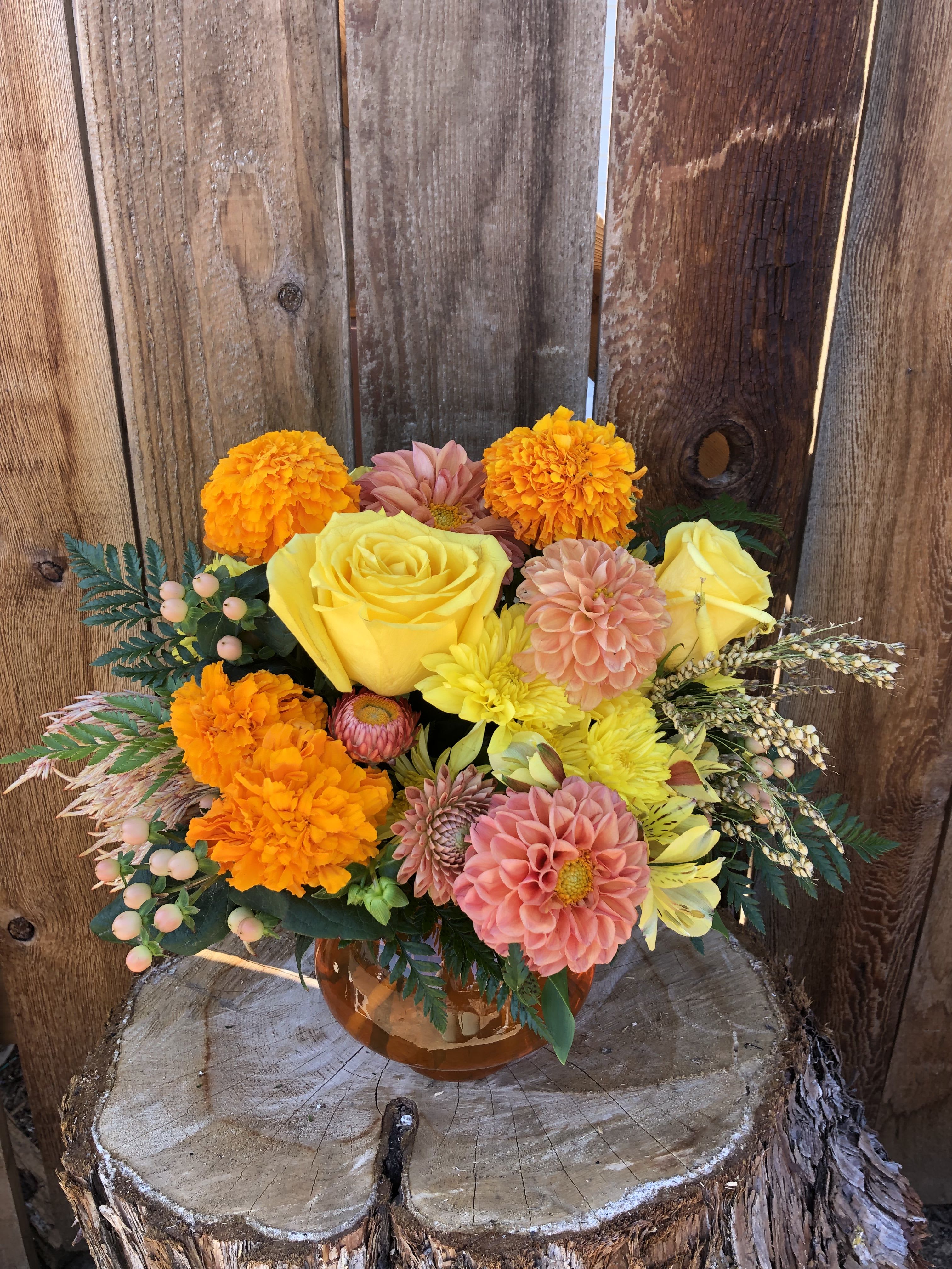 Bouquet of yellow roses, orange marigolds, and pink dahlias in an amber vase