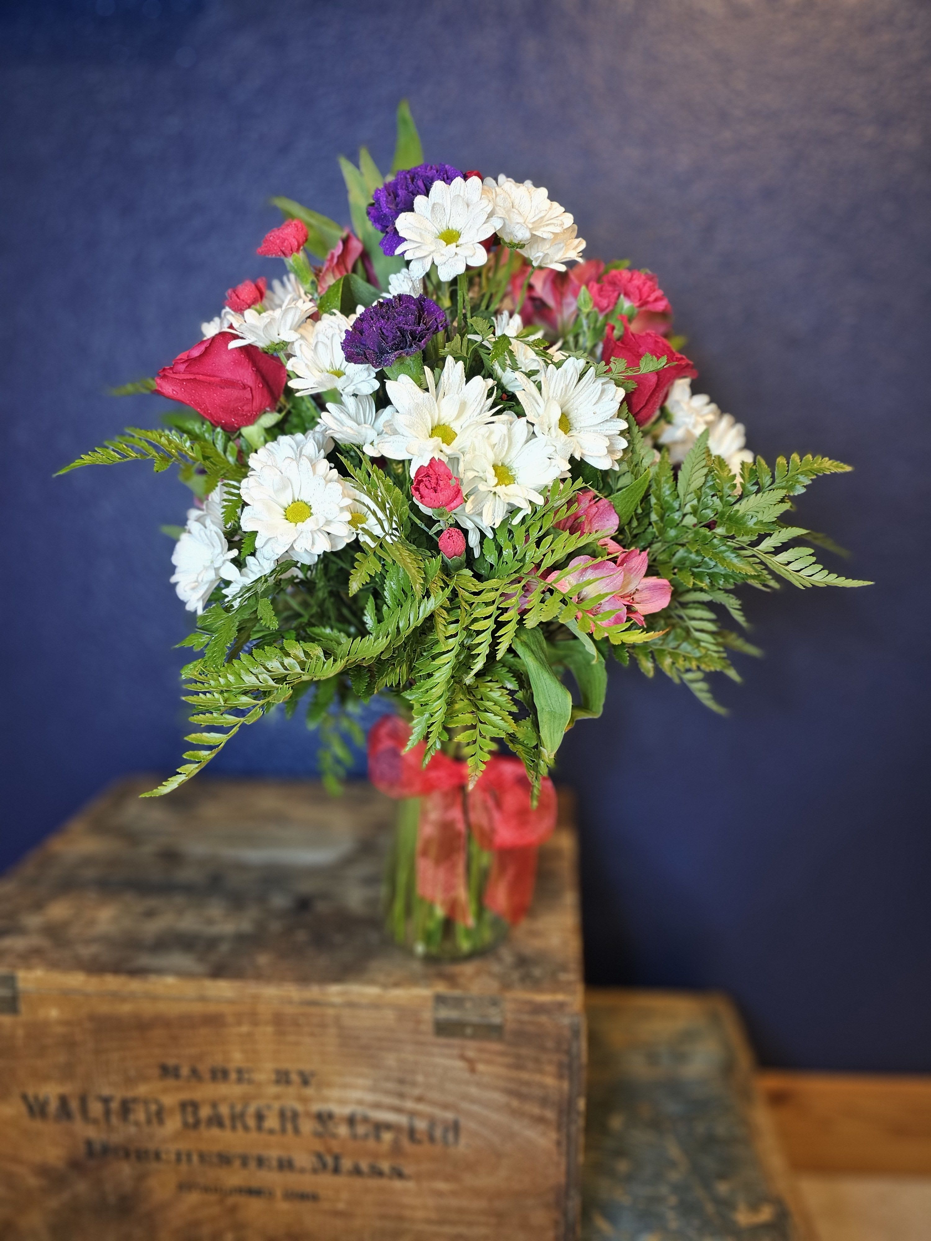 Bouquet of white daisies, pink roses, and purple blooms in a glass vase