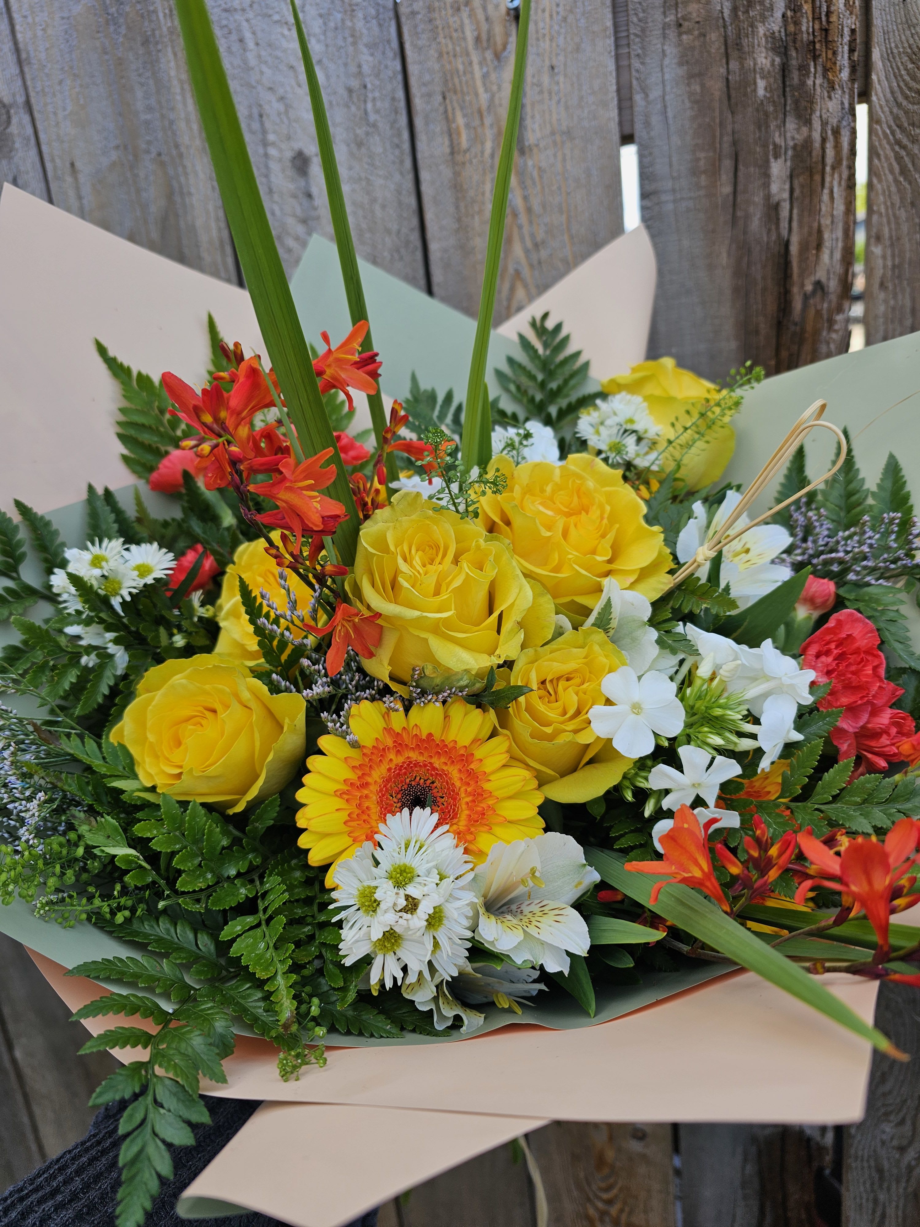 Bouquet of yellow roses, orange gerbera daisies, and white flowers wrapped in paper