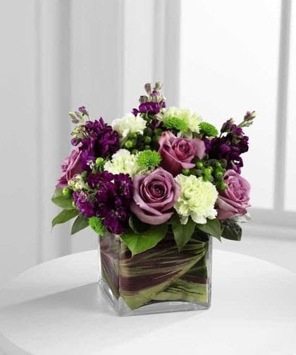Purple and white floral arrangement in a square glass vase