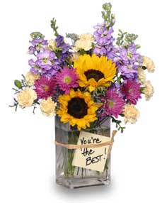 Bouquet of sunflowers, purple flowers, and cream blooms in a glass vase