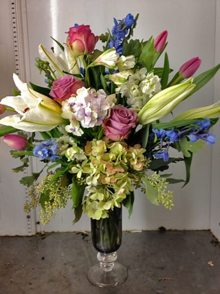 Bouquet of pink roses, white lilies, and blue flowers in a glass vase