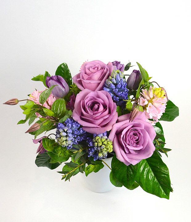 Lavender roses with purple tulips and blue flowers in a white vase