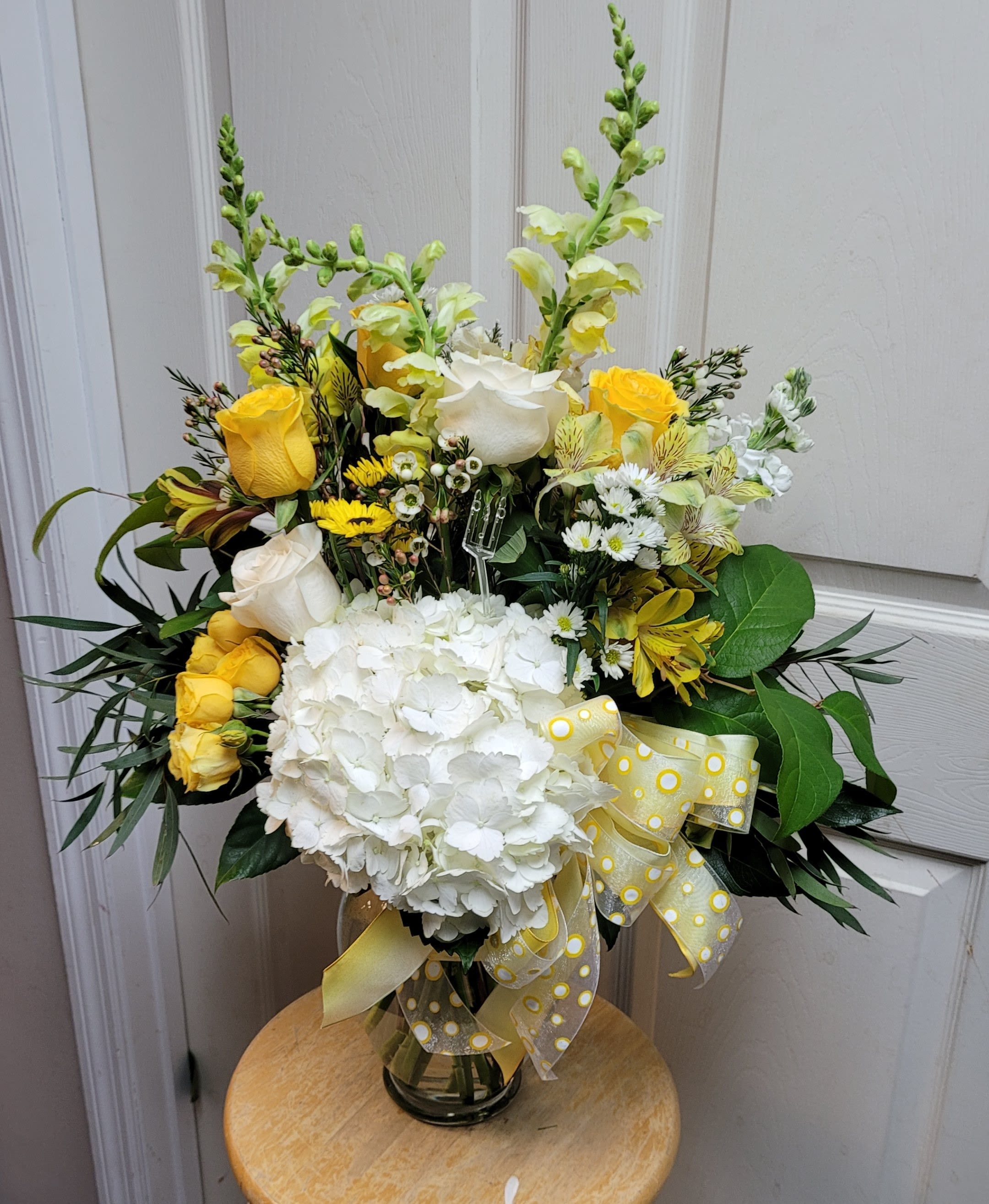 Yellow and white floral arrangement in a glass vase with a ribbon