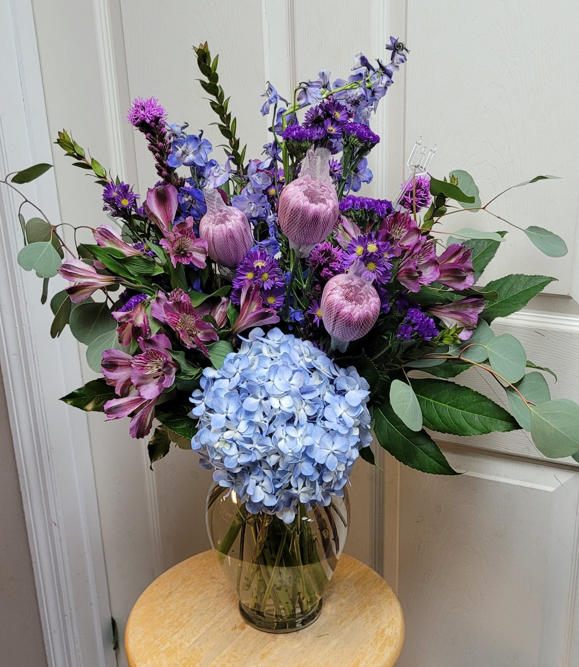 Bouquet of blue hydrangea, purple flowers, and pink alstroemeria in a glass vase