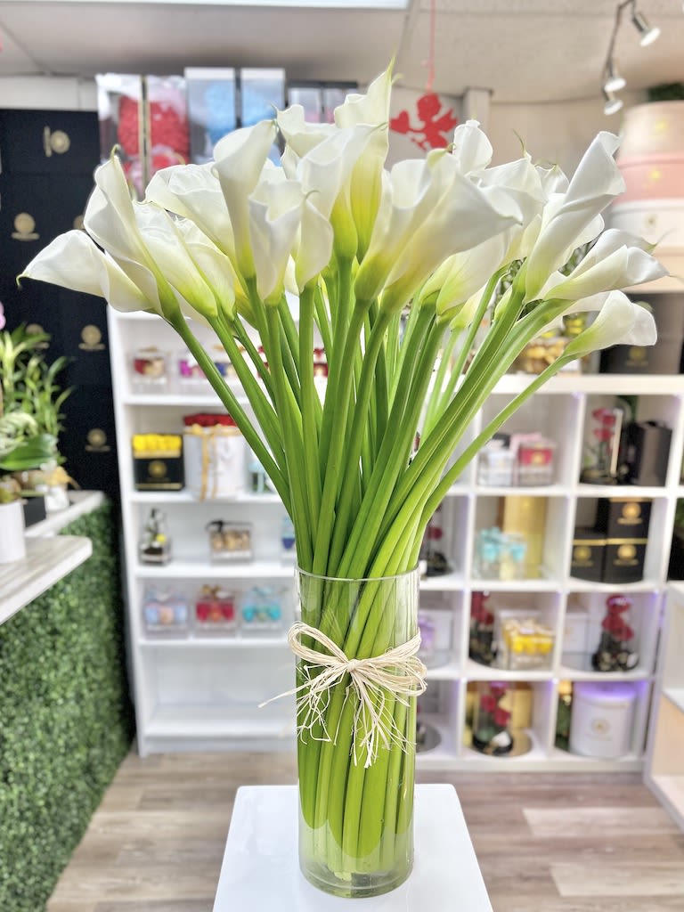 Tall bundle of white calla lilies in a clear glass vase tied with raffia