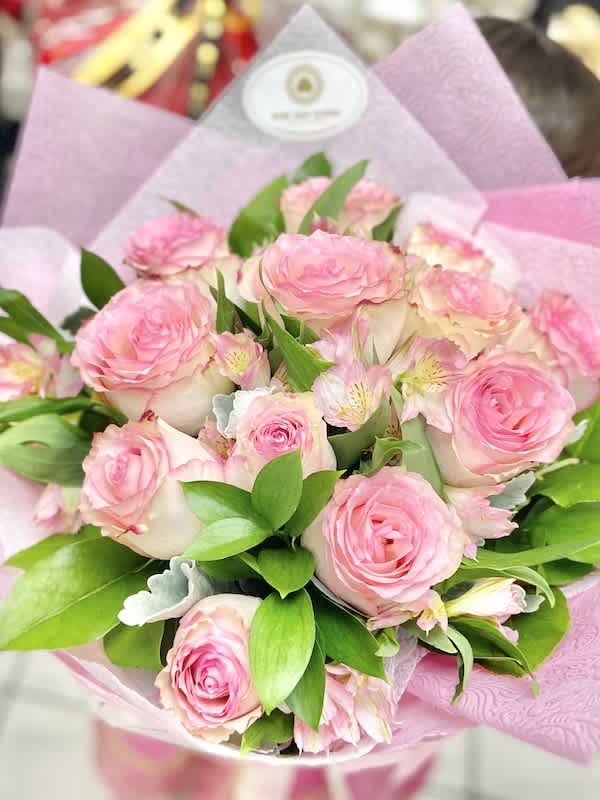 Hand-tied bouquet of pink roses and pale pink blooms wrapped in pink paper