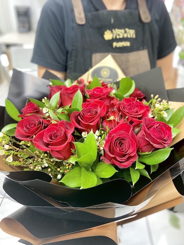 Hand-tied bouquet of red roses with small white filler flowers in black and tan wrap