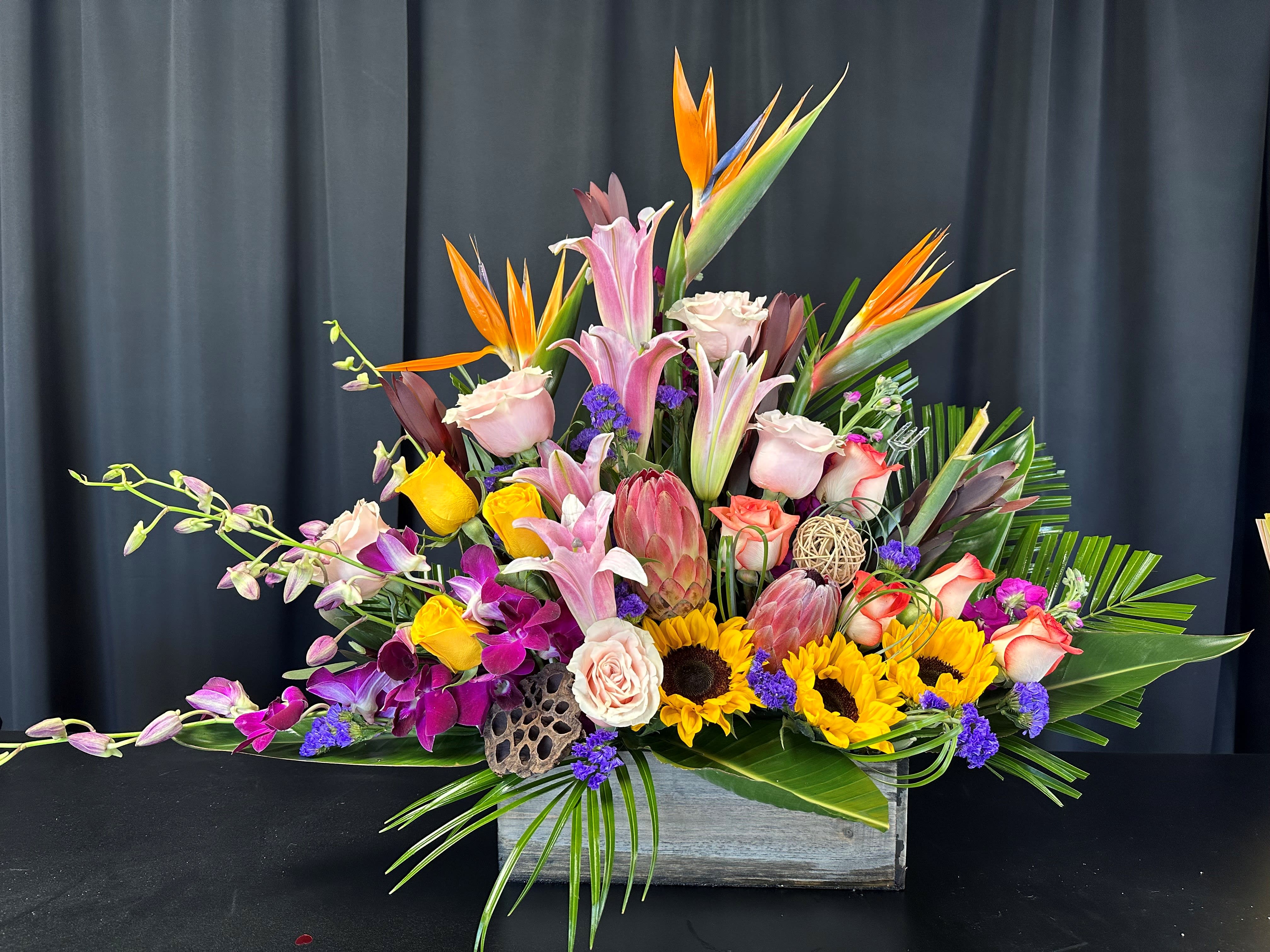 Tropical flower arrangement with lilies, roses, orchids, and sunflowers in a wooden box
