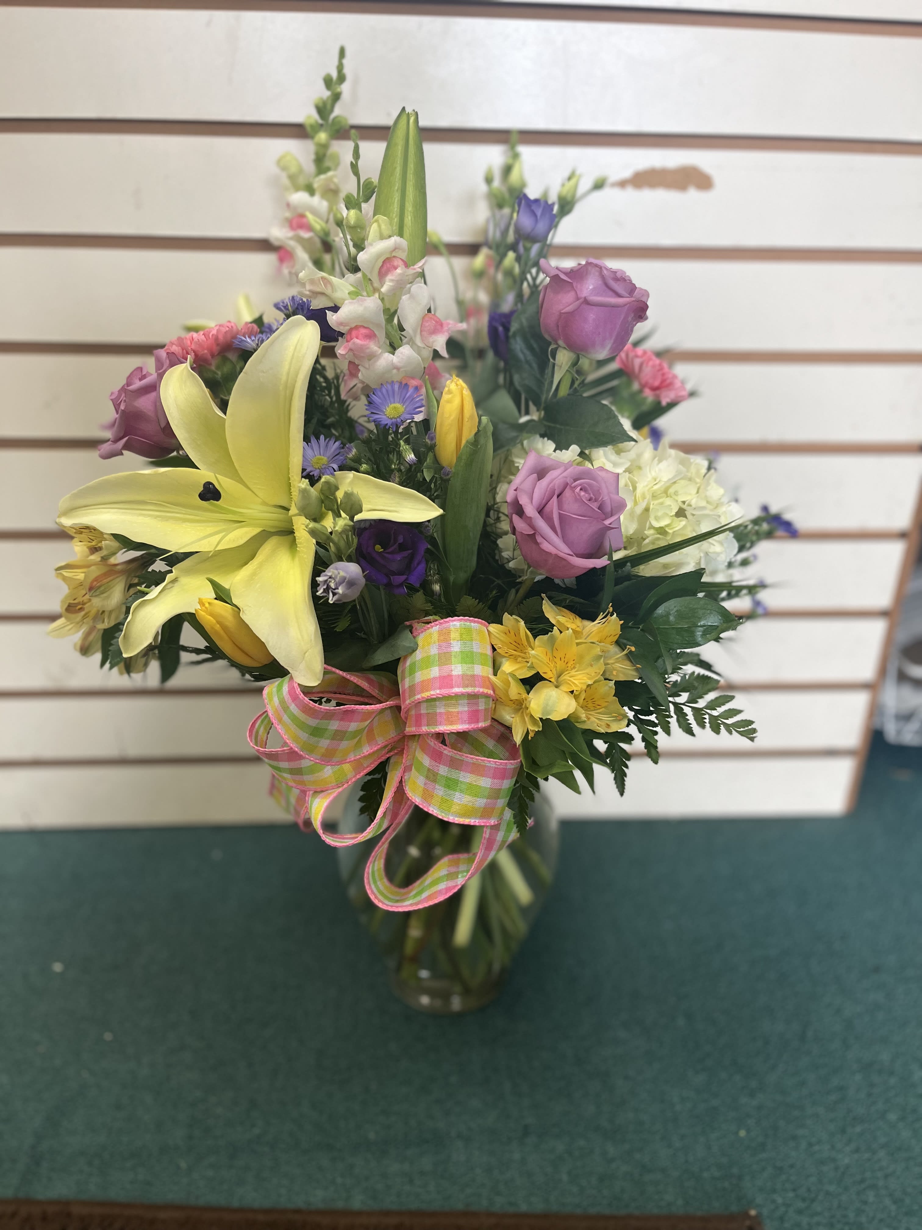 Mixed bouquet with yellow lilies, pink roses, and a plaid ribbon in a glass vase